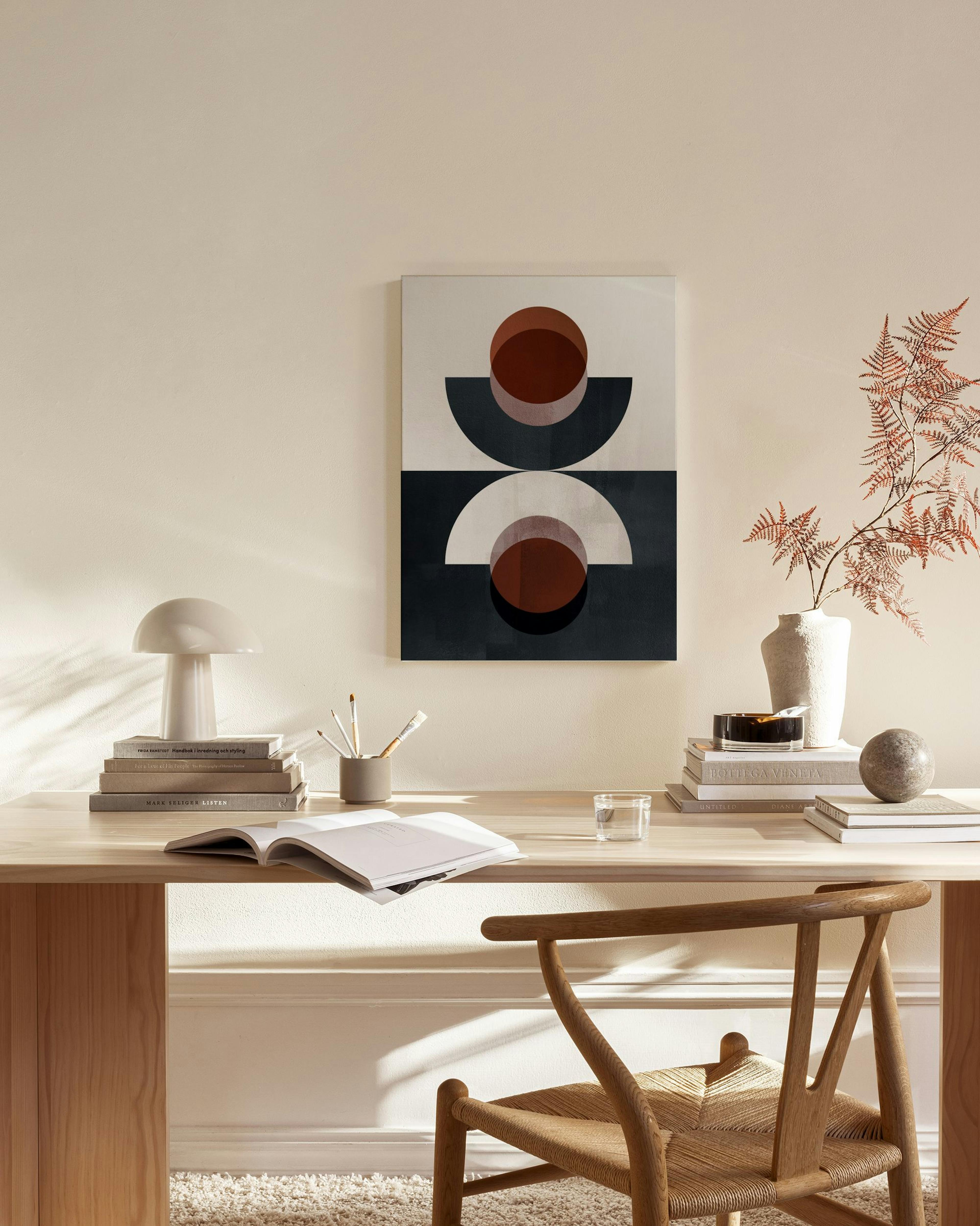 Lienzo geométrico con semicírculos y círculos en tonos tierra y oscuros, colgado sobre un mueble bajo en un salón moderno.