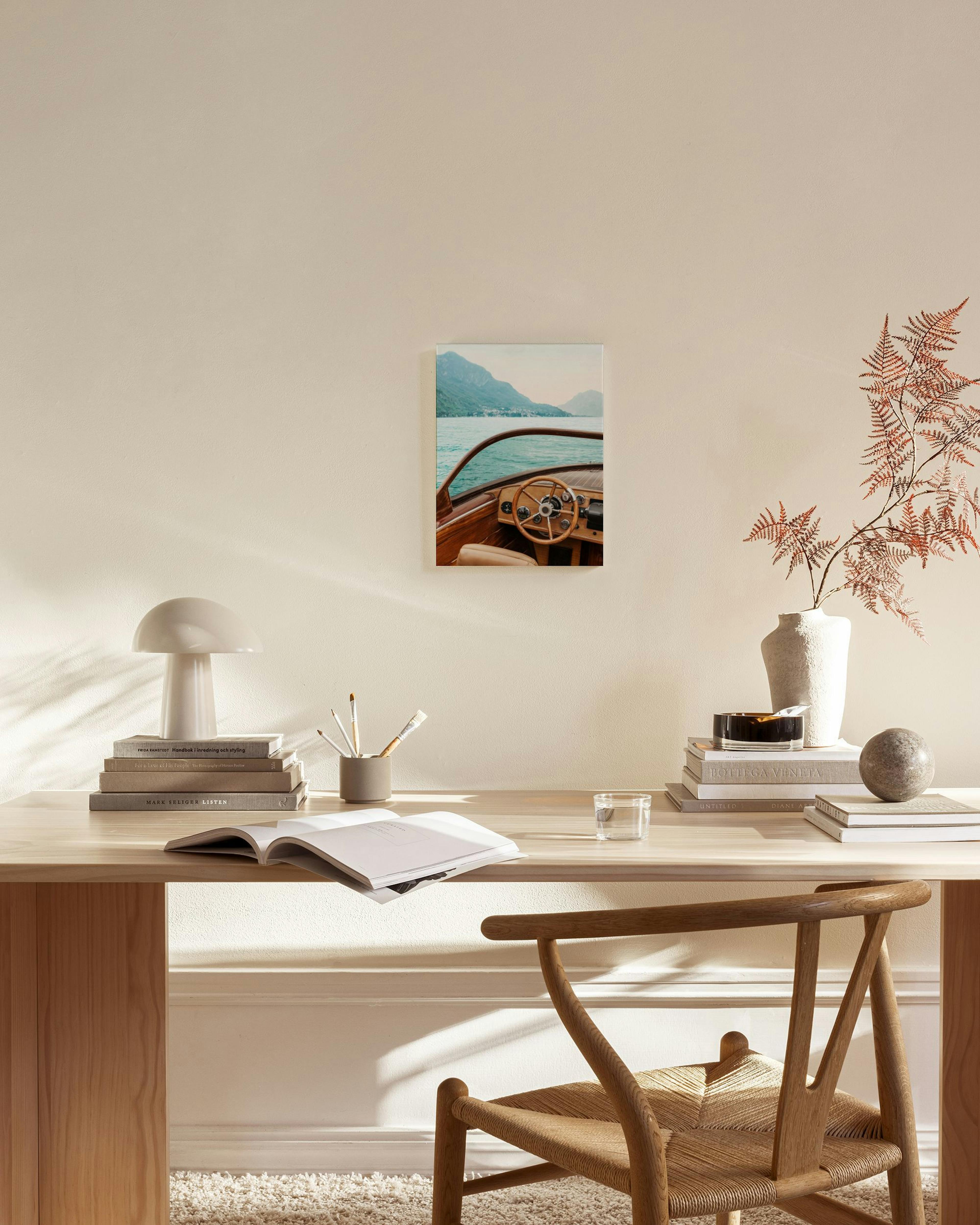 A canvas print of a wooden boat on a lake with mountains in the background, displayed in a bright living room.