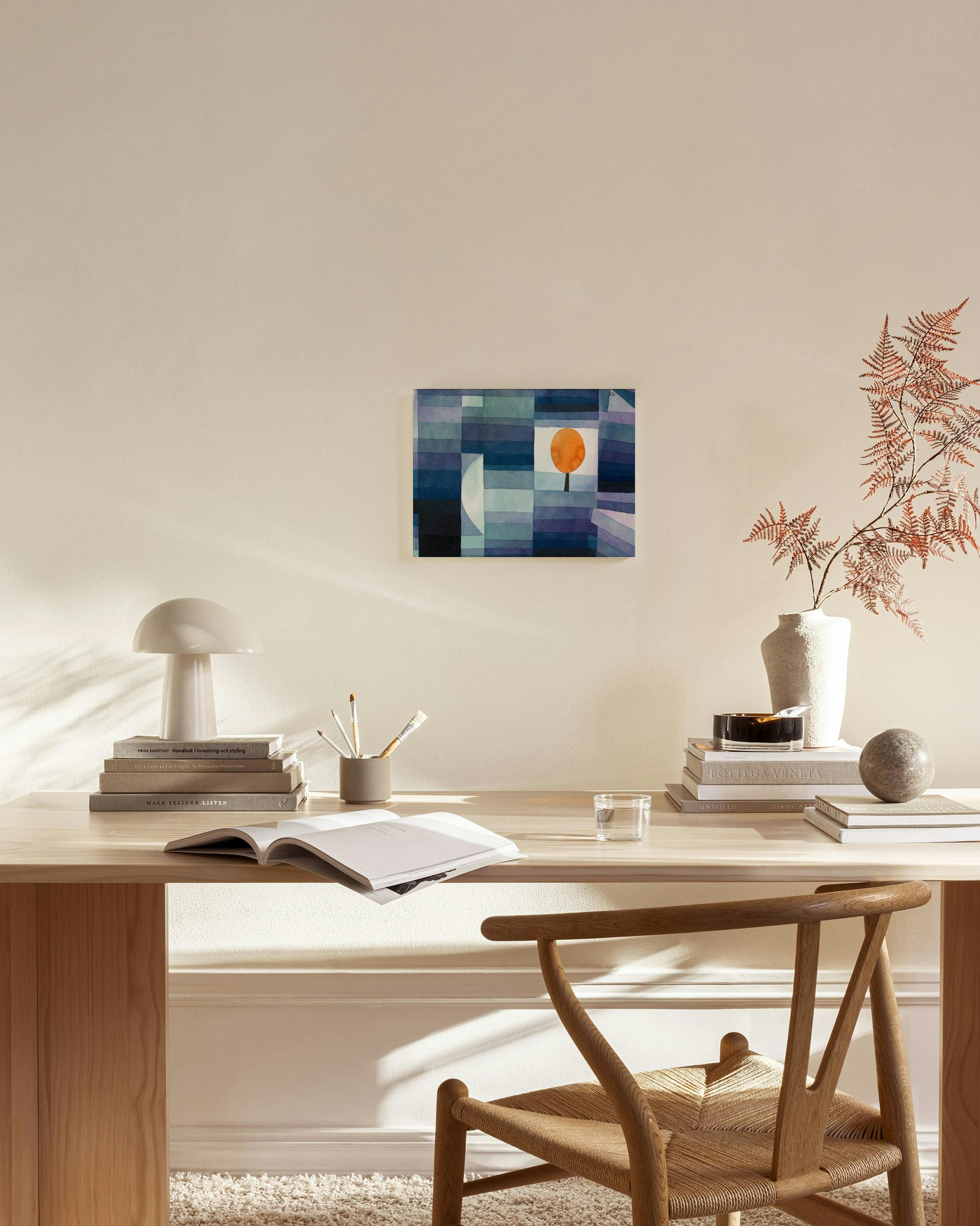 Sinisävyinen kanvaasi, jossa oranssi aurinko ja tumma puu, ripustettuna moderniin olohuoneeseen.