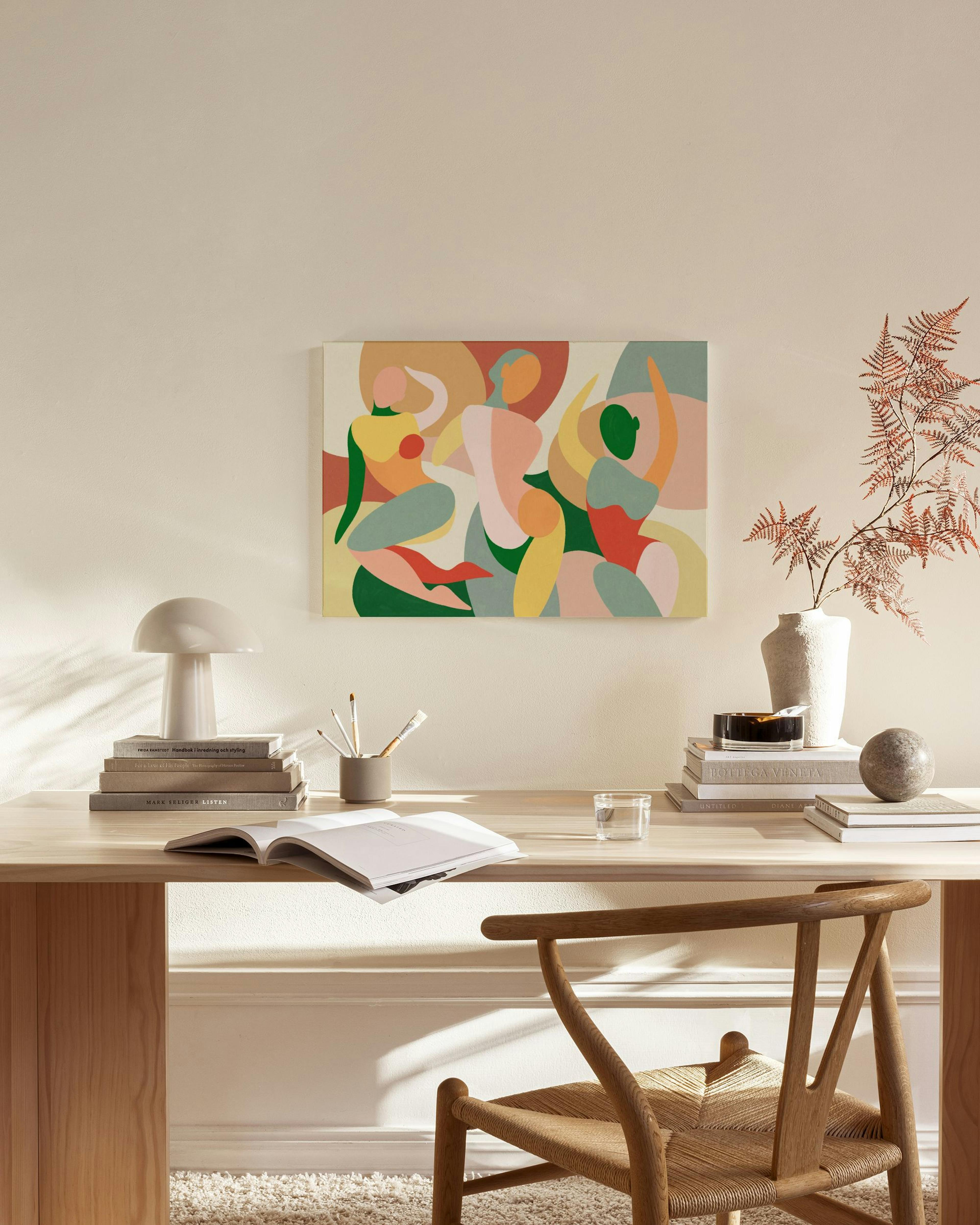 Lærred med abstrakte figurer i grønne, gule og rosa nuancer, hængende i en stue over et træmøbel.
