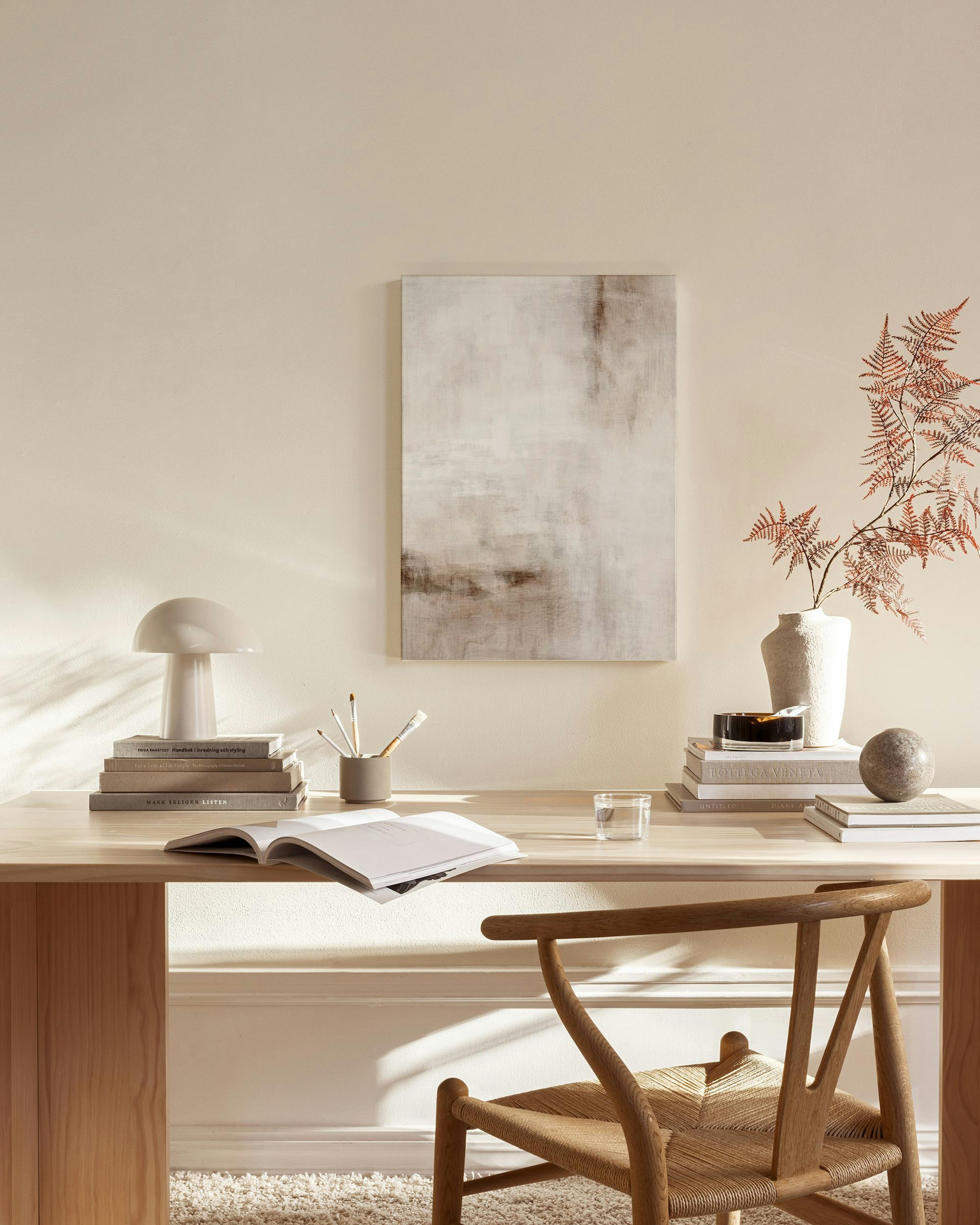 Lienzo abstracto con formas orgánicas en tonos beige y marrón, colgado sobre un mueble de madera y una silla en una sala.