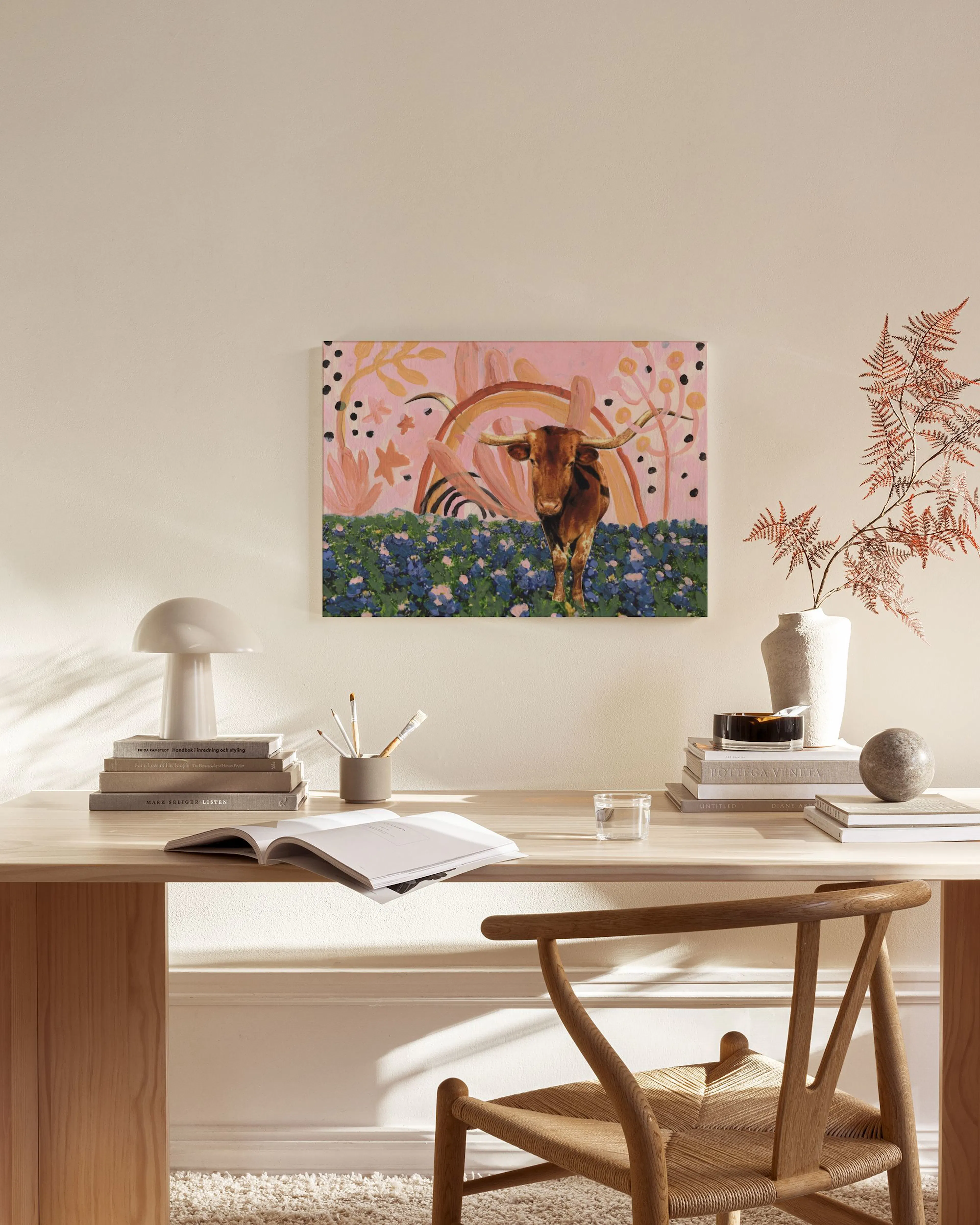 A colorful canvas print of a longhorn in a field of bluebonnets with a rainbow, displayed in a bright living room.