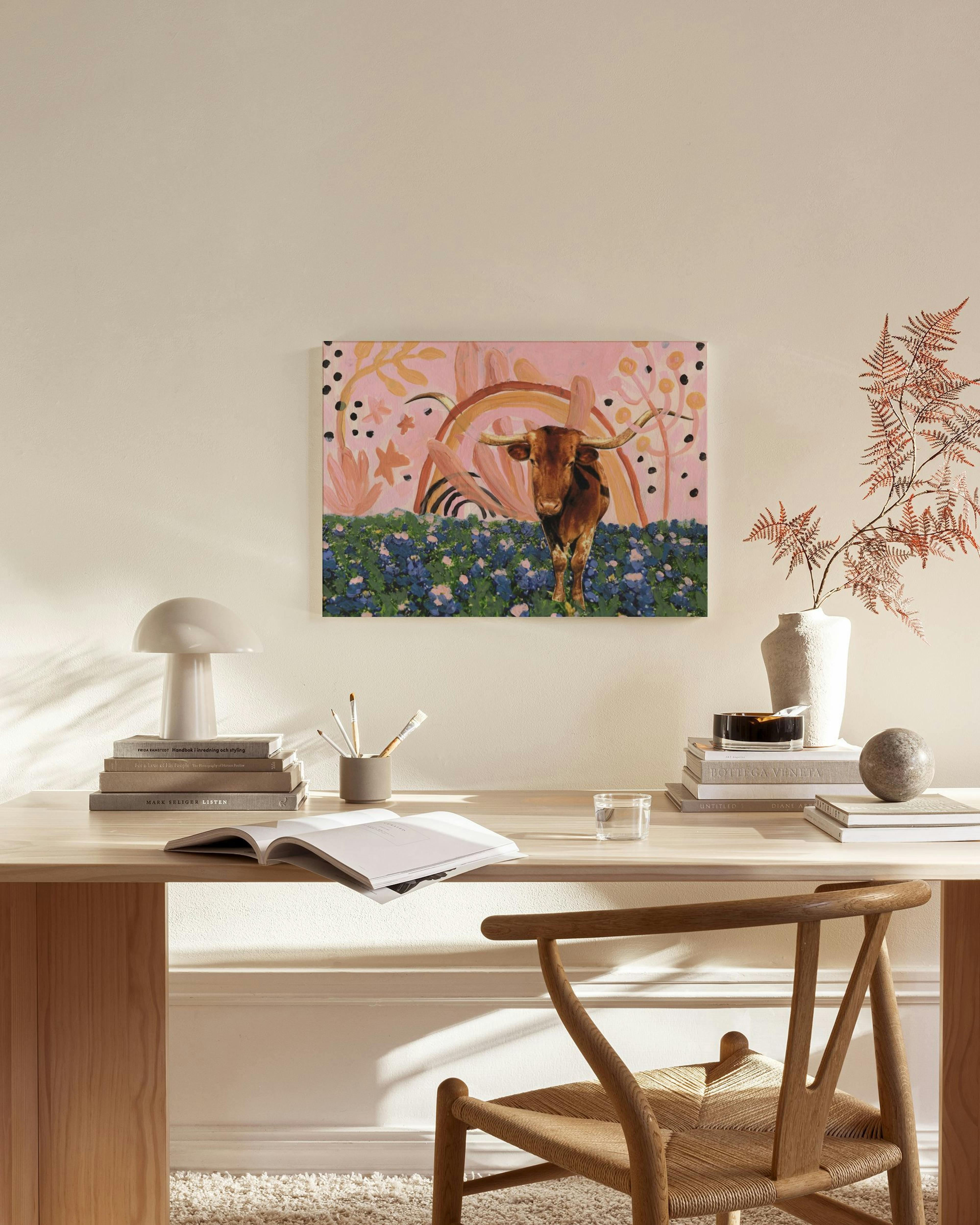 Obraz na płótnie przedstawiający brązowego byka na tle różowego nieba z tęczą i kwiatami, wiszący w salonie.