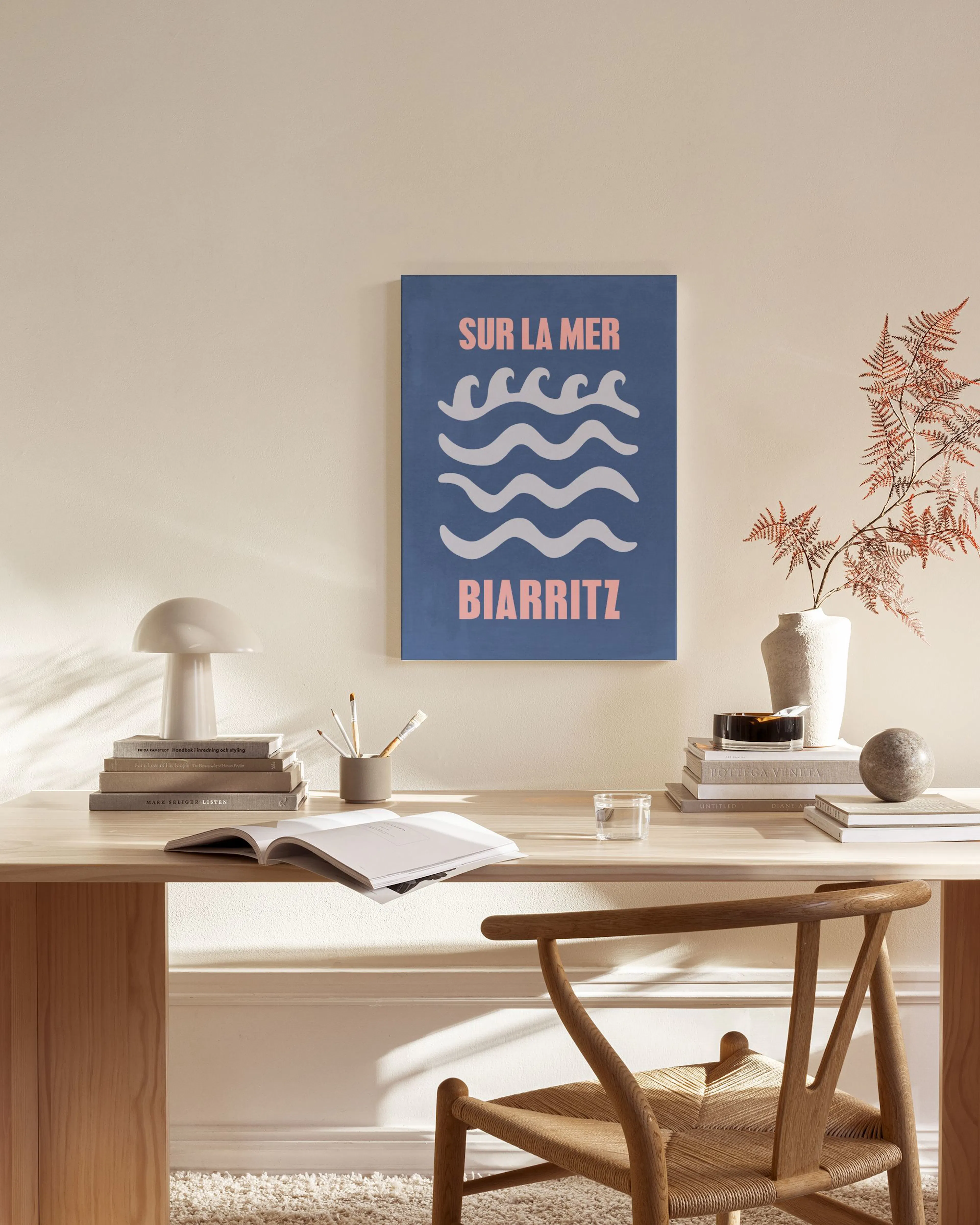 Toile SUR LA MER BIARRITZ bleue avec vagues blanches et texte rose, accrochée dans un salon bohème.