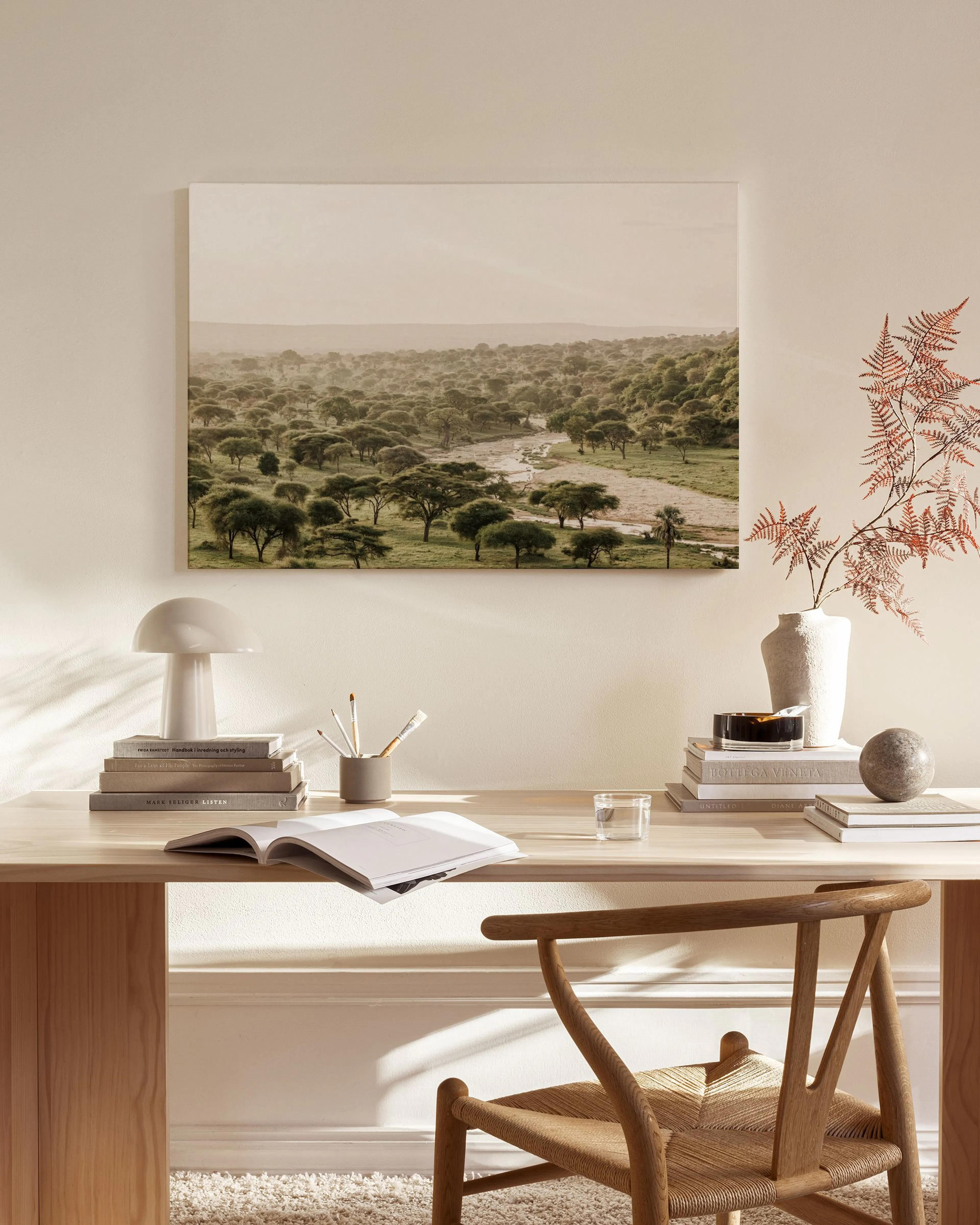 A landscape print of a river flowing through green trees, displayed above a wooden console table in a neutral-toned living room.