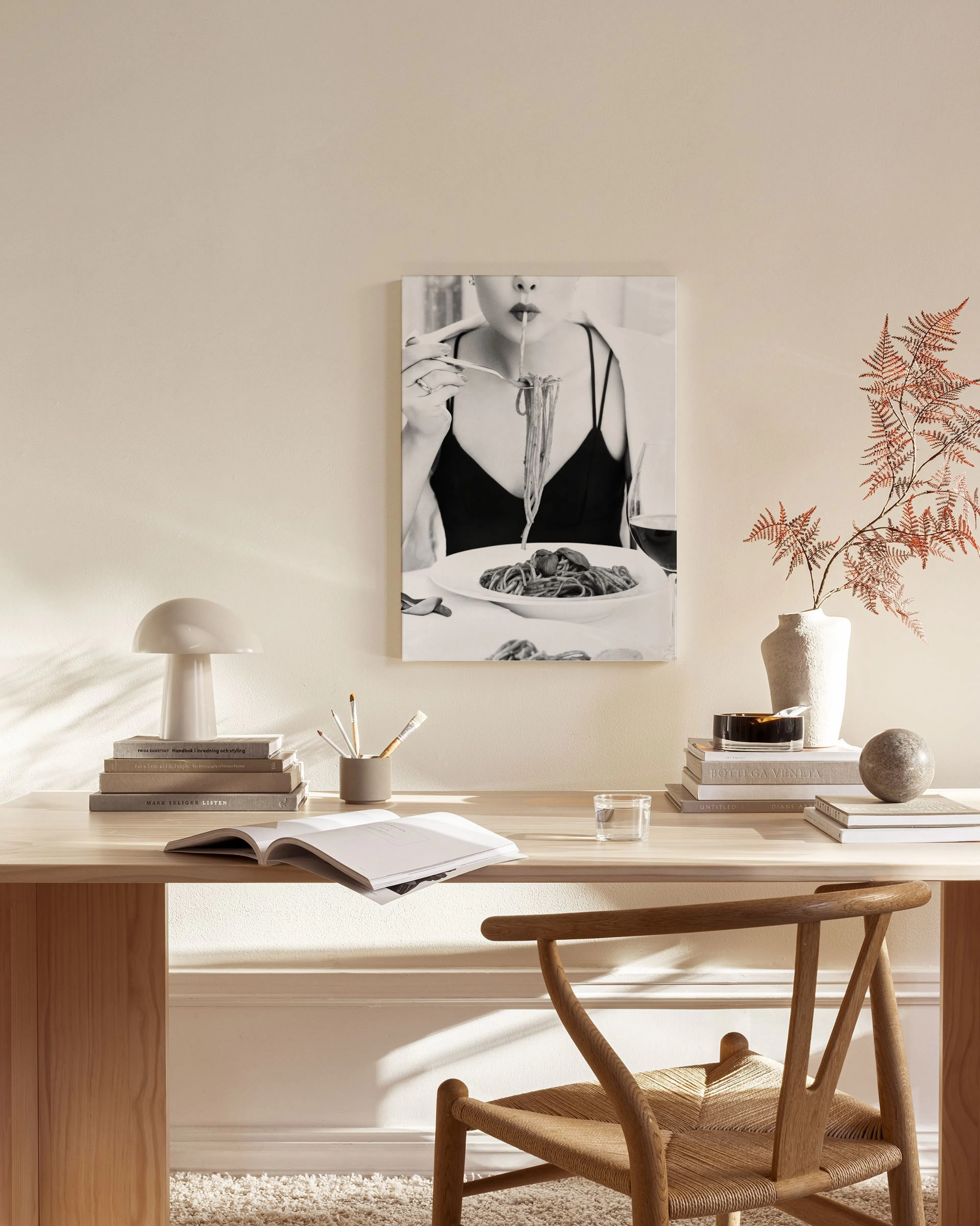 Schwarz-weiß Leinwandbild einer Frau beim Spaghetti-Essen, hängend über einem Sideboard in einem beigen Wohnzimmer.