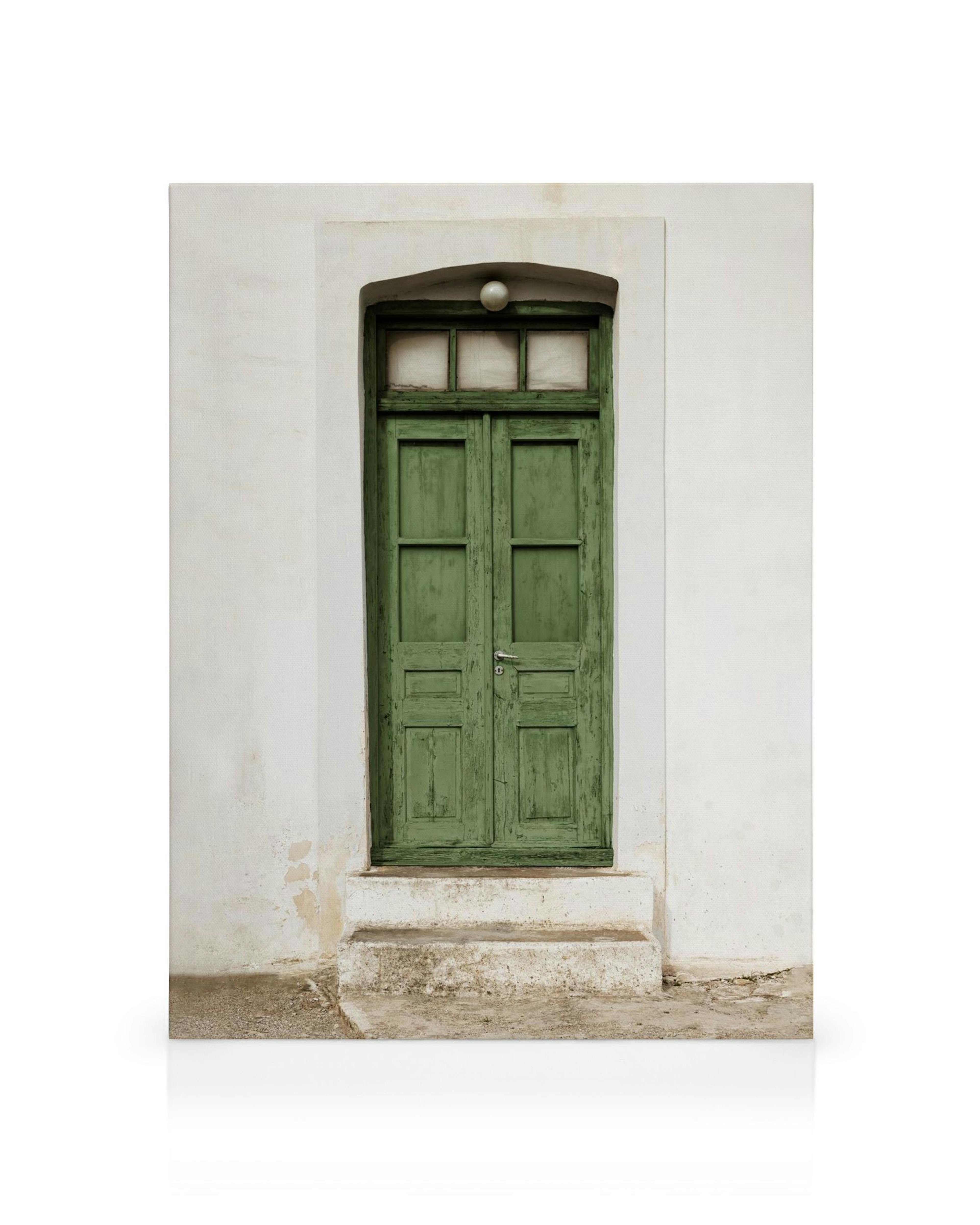 Puerta de madera verde con pintura descascarada en una pared blanca, con ventana semicircular y escalones rústicos.