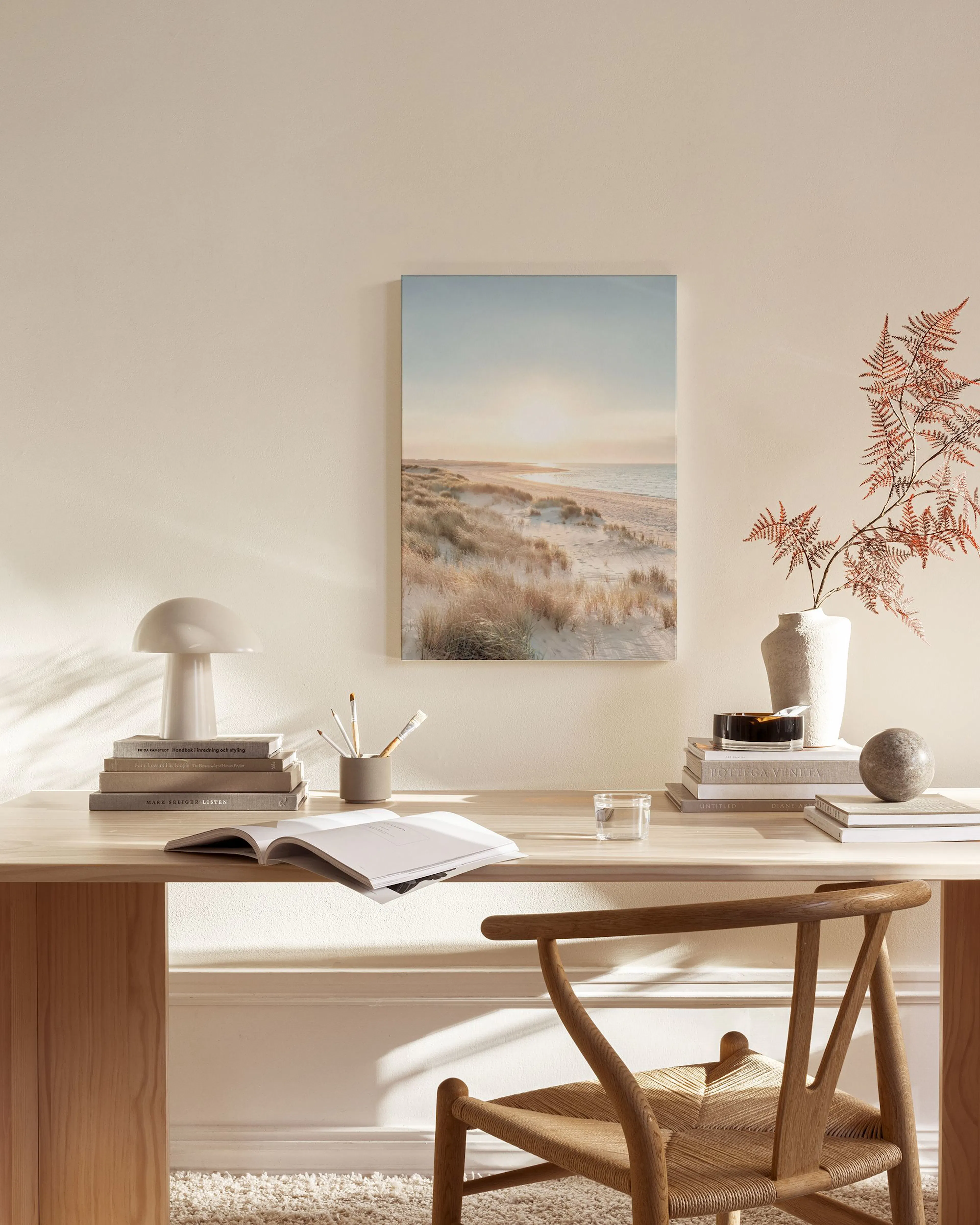 A canvas print of a sandy beach and ocean at sunset, hanging in a minimalist living room above a wooden console.