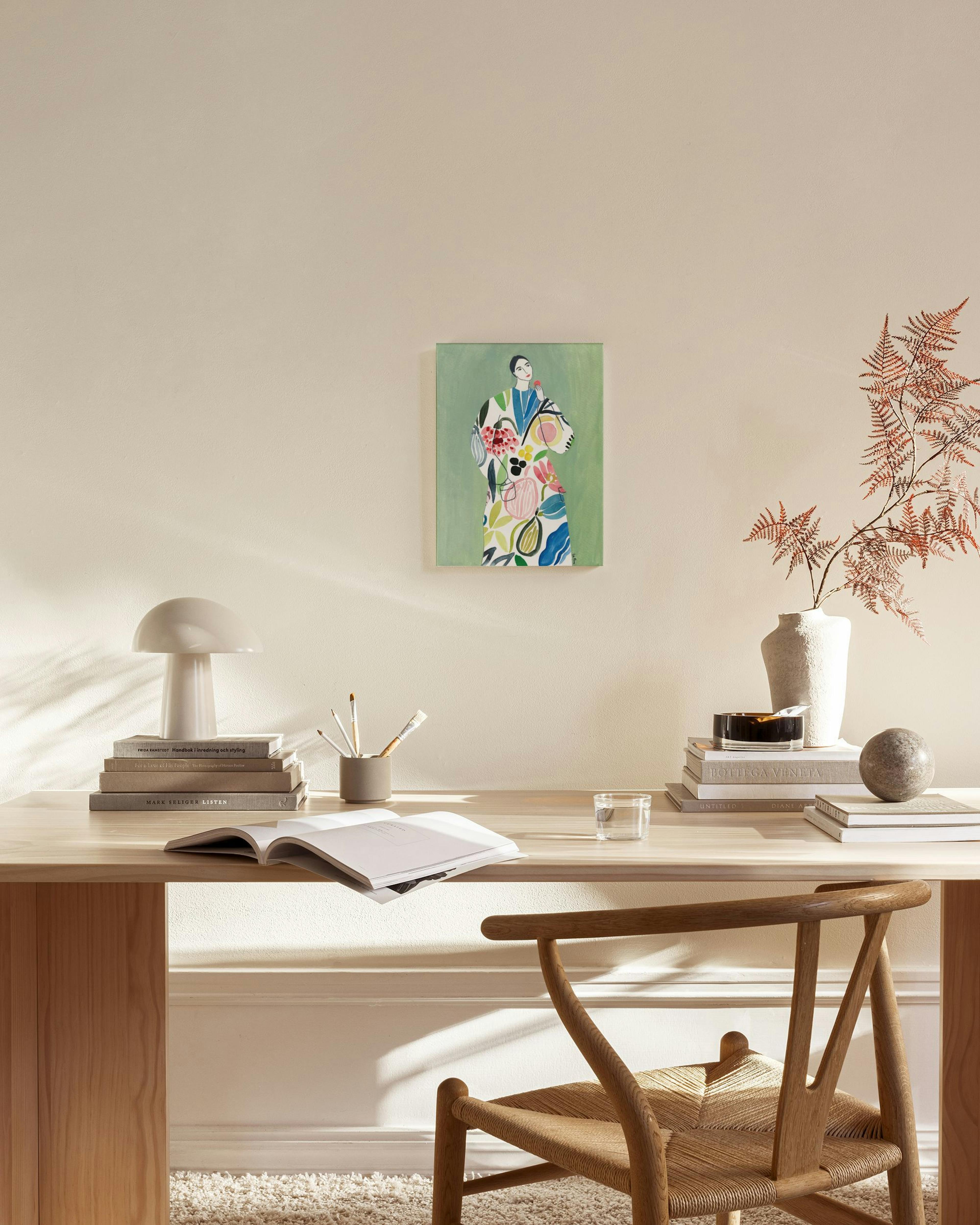 A canvas print of a woman in a colorful floral-patterned dress on a green background, hanging in a modern living room.