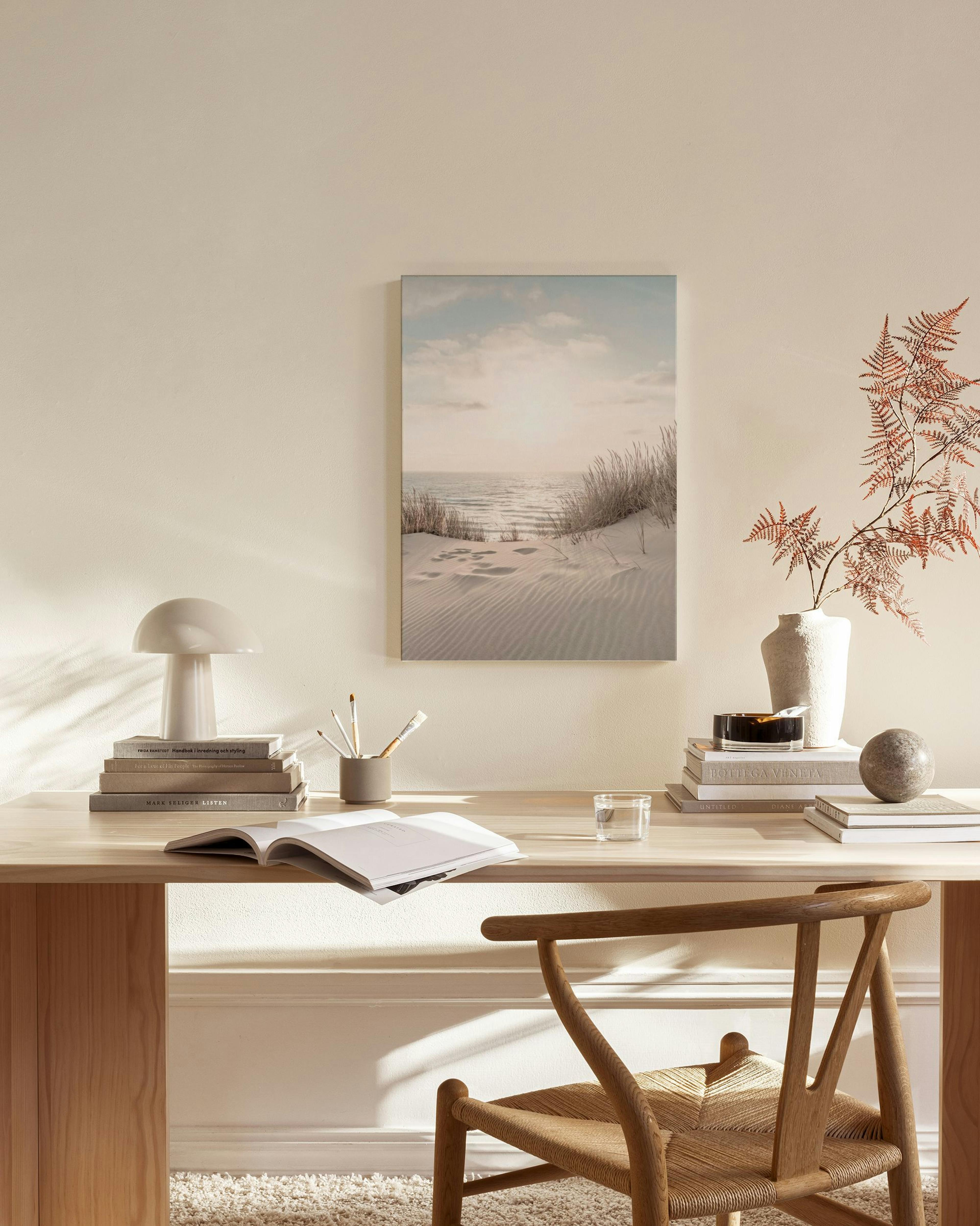 Stampa su tela di dune di sabbia con impronte e mare al tramonto, appesa in un soggiorno moderno.