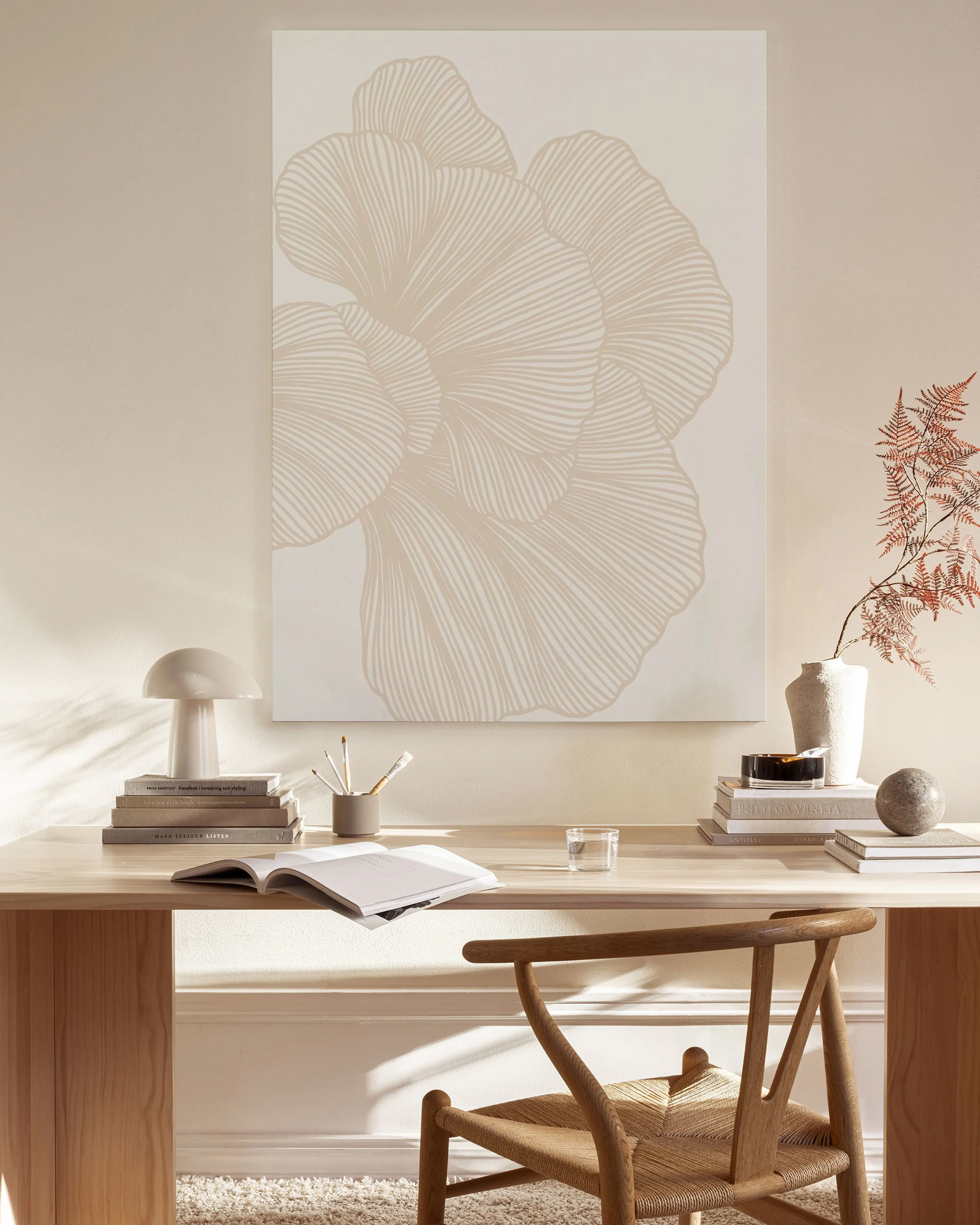 Tela decorativa com desenho abstrato de pétalas em tons de bege, pendurada numa sala de estar minimalista com móveis de madeira.