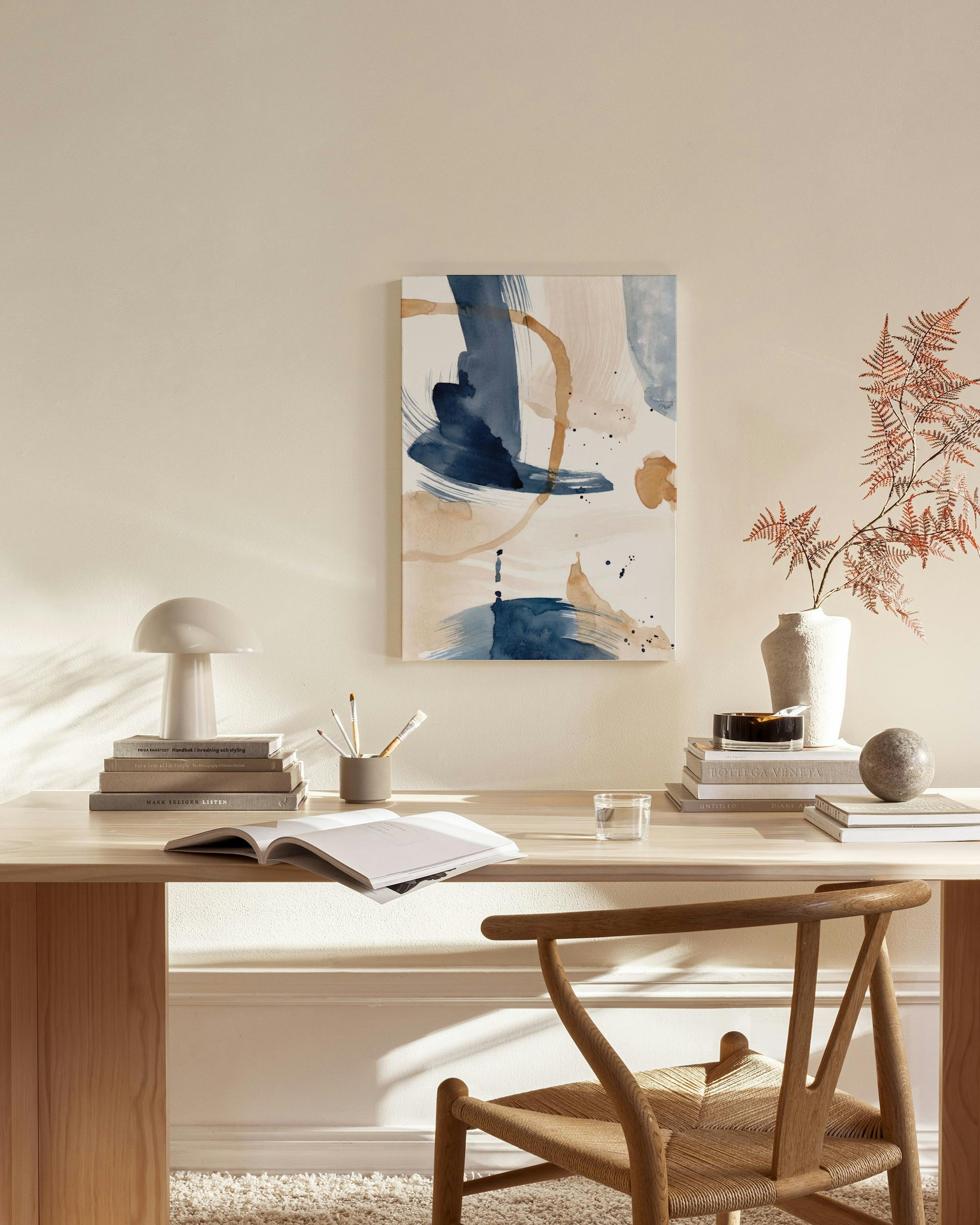 Abstrakti kanvaasi sinisen, beigen ja oranssin sävyissä modernissa olohuoneessa puisen tuolin yläpuolella.