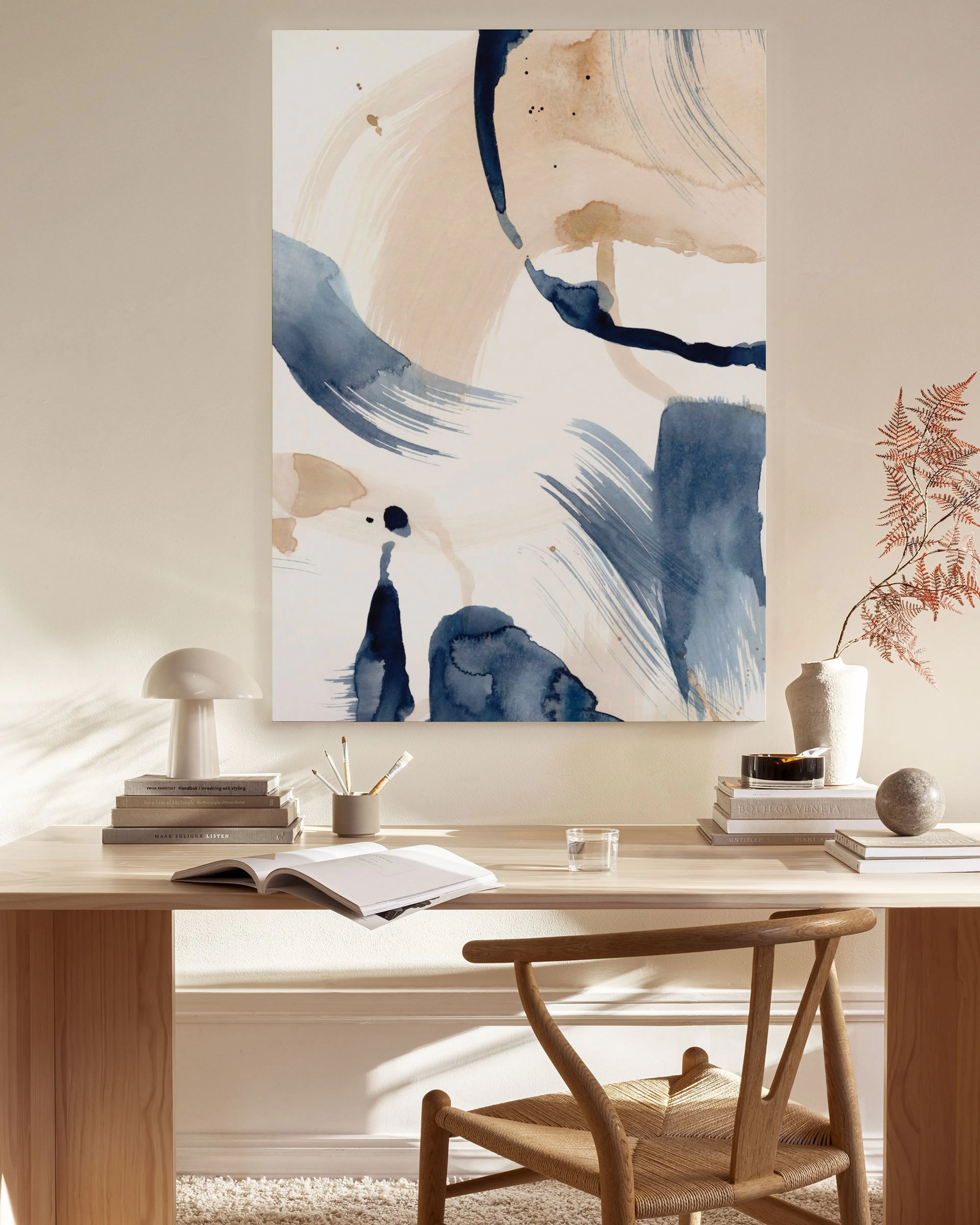Abstract canvas print with navy and beige brushstrokes, and white highlights, hanging in a light-filled living room.