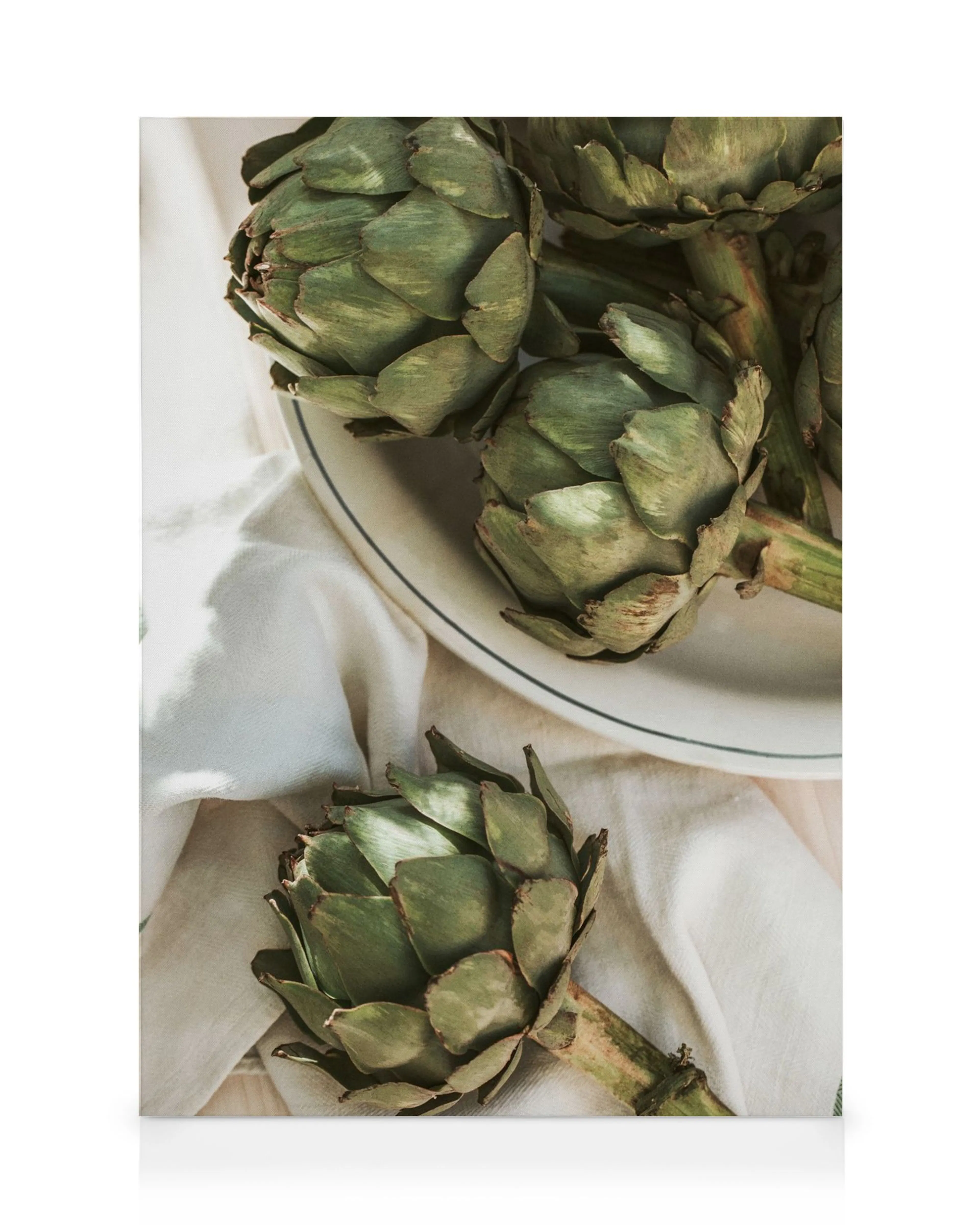 Lienzo de alcachofas frescas en un plato blanco con borde azul y un paño arrugado.