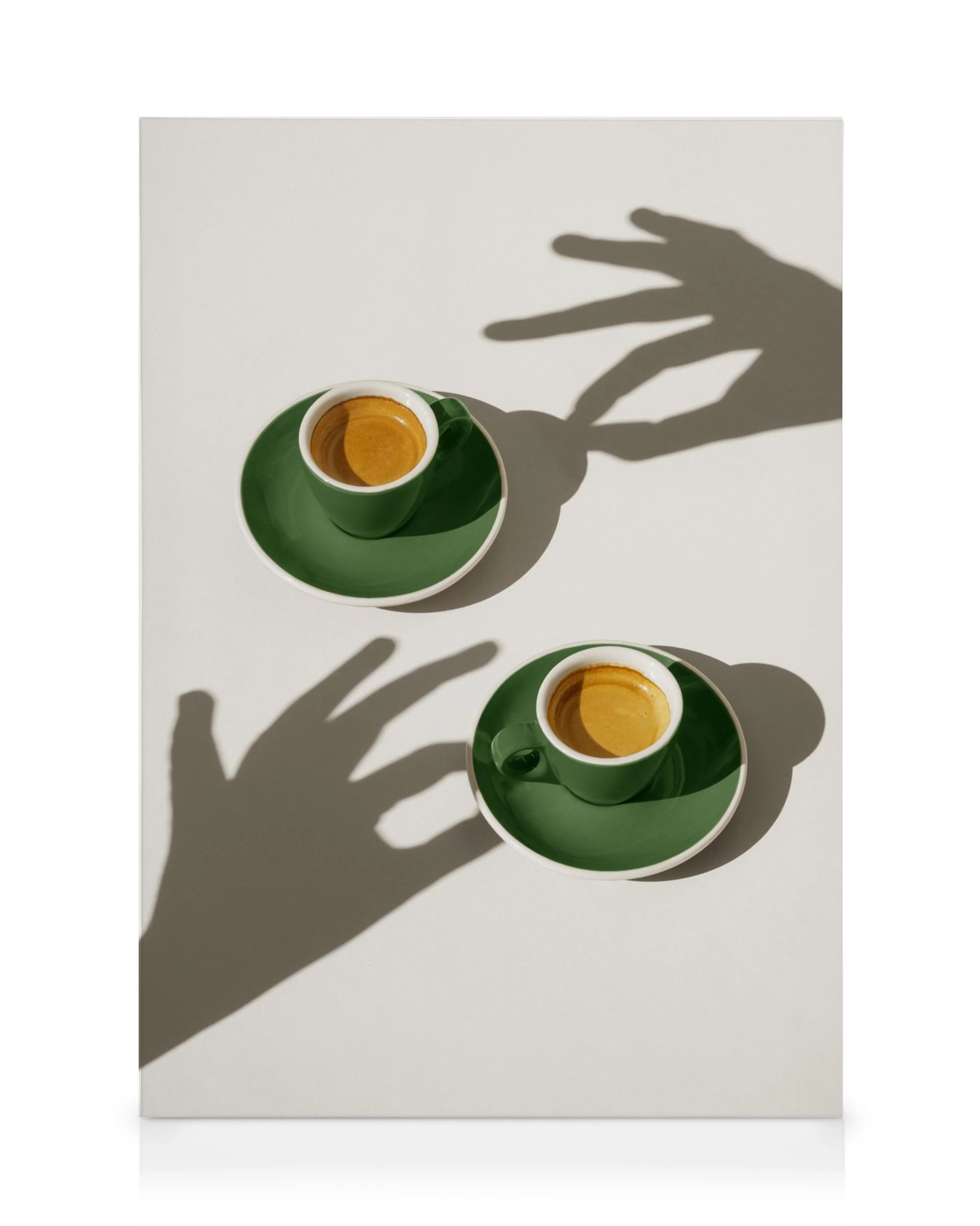 Leinwandbild mit zwei grünen Espressotassen und Untertassen auf weißem Hintergrund, begleitet von Hand-Schatten.