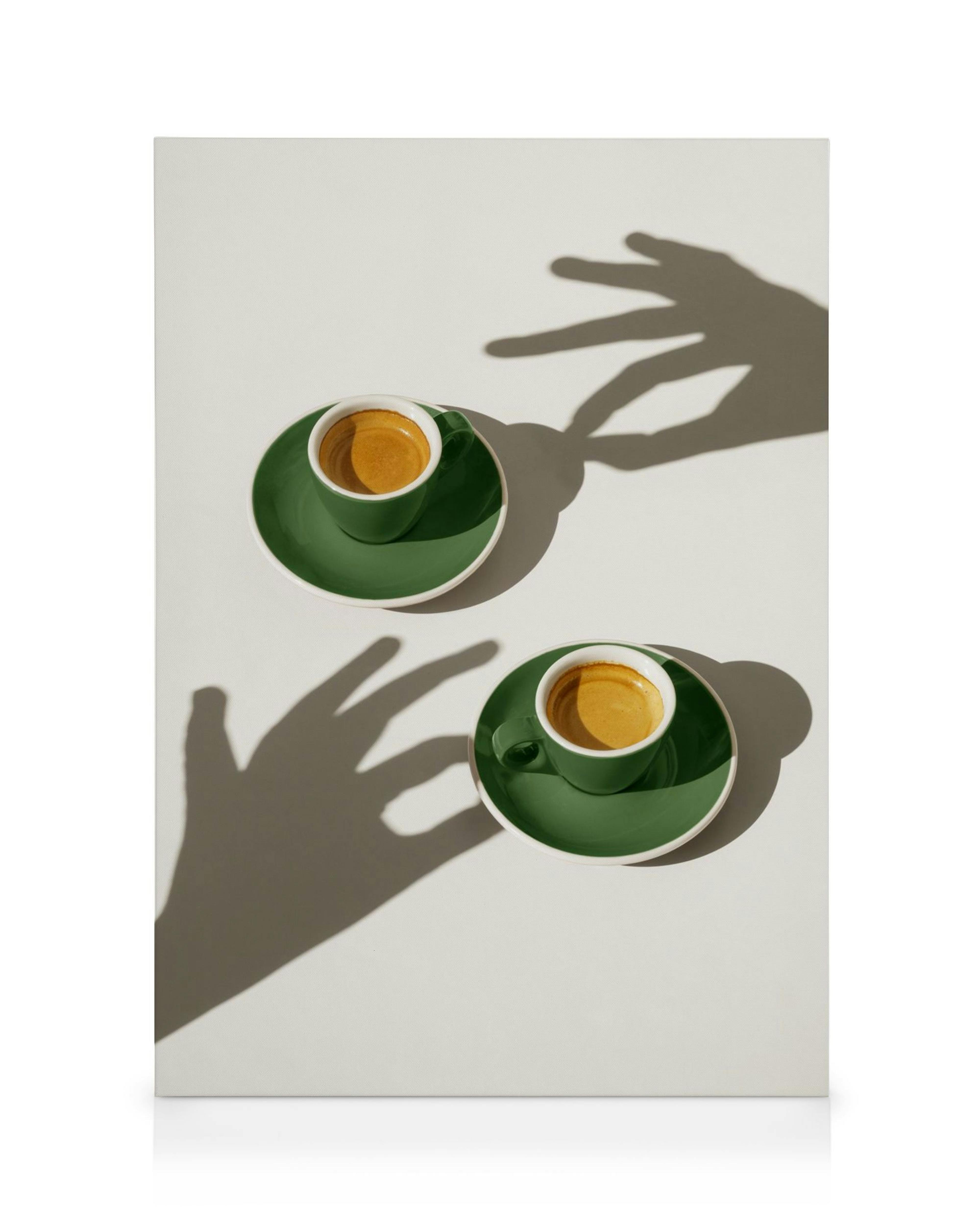 Toile avec deux tasses de café vert foncé sur fond blanc et ombres de mains.