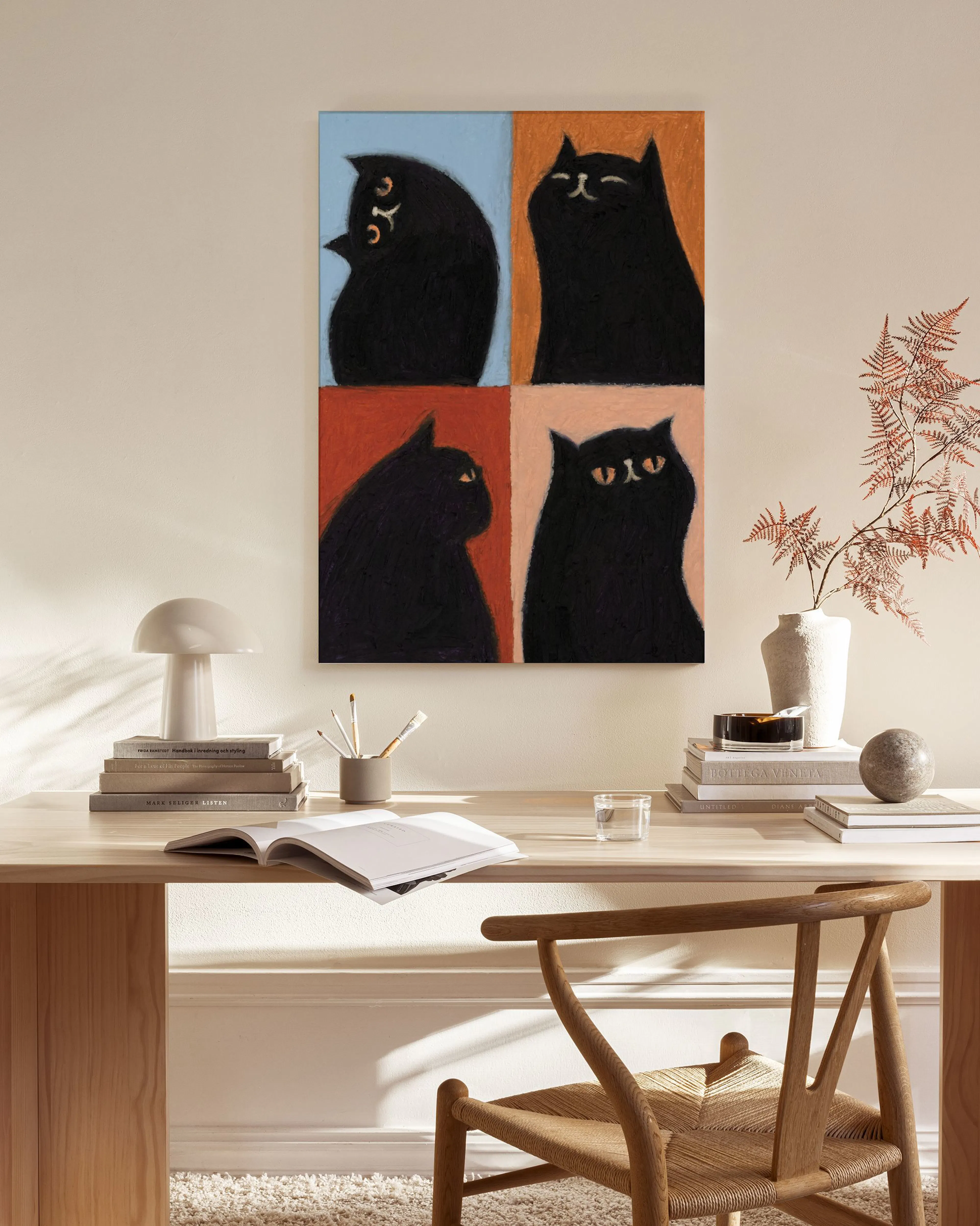 A canvas print of four black cats on colorful backgrounds, displayed on a beige wall in a modern living room.