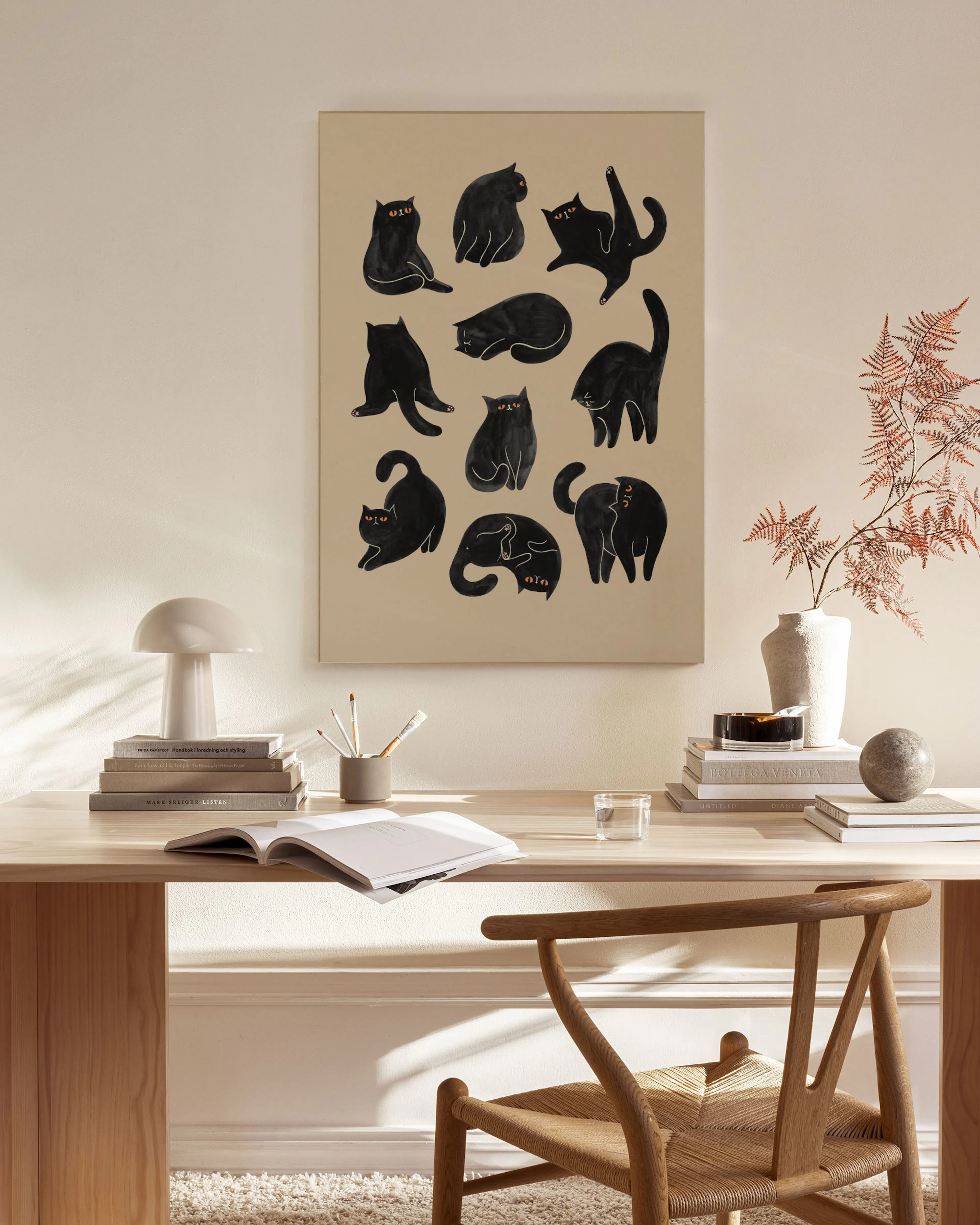 A canvas print of black cartoon cats on a beige background, hanging in a minimalist living room.