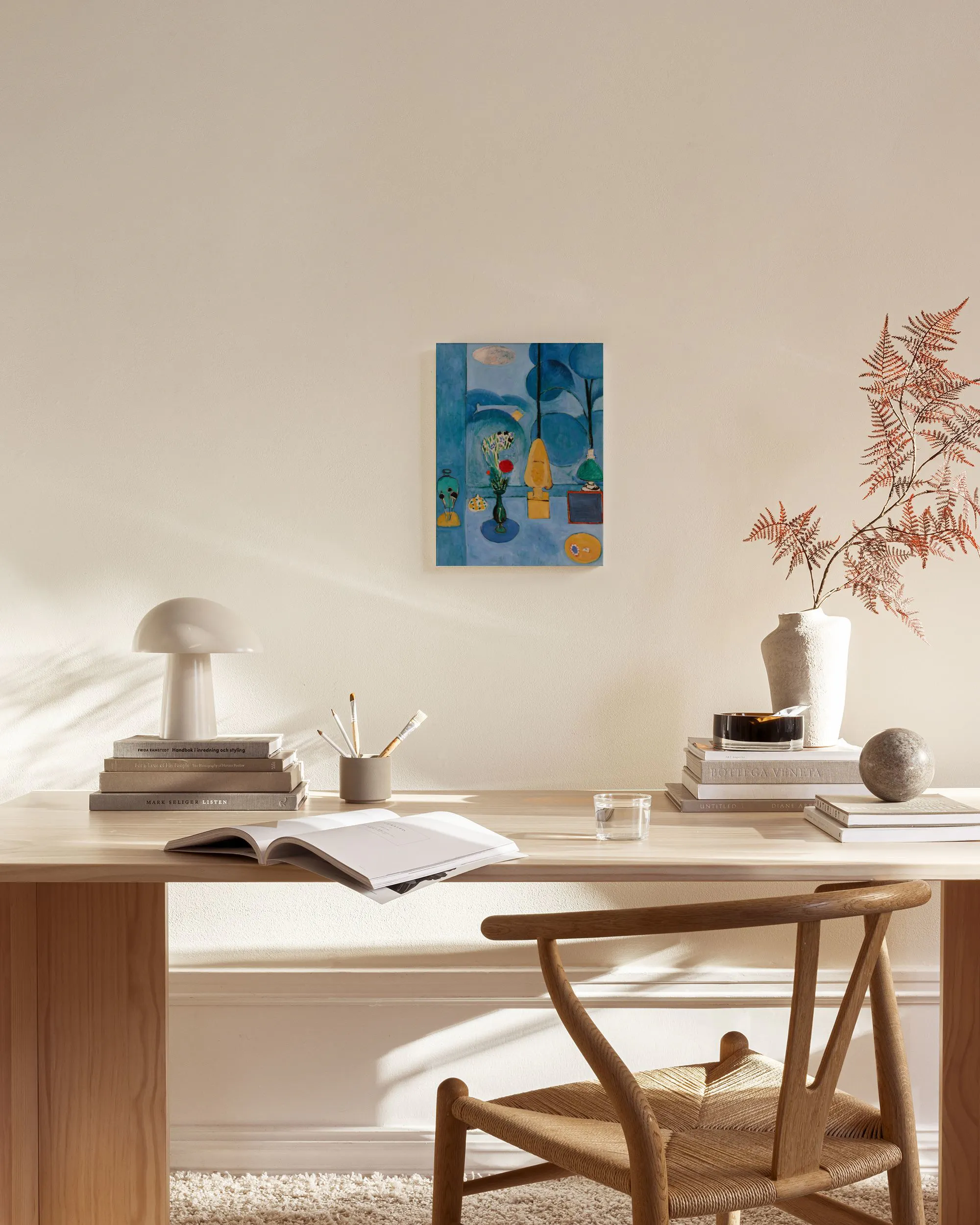 Een canvas met een blauw stilleven van vazen, planten en fruit, hangend boven een houten dressoir in een moderne woonkamer.