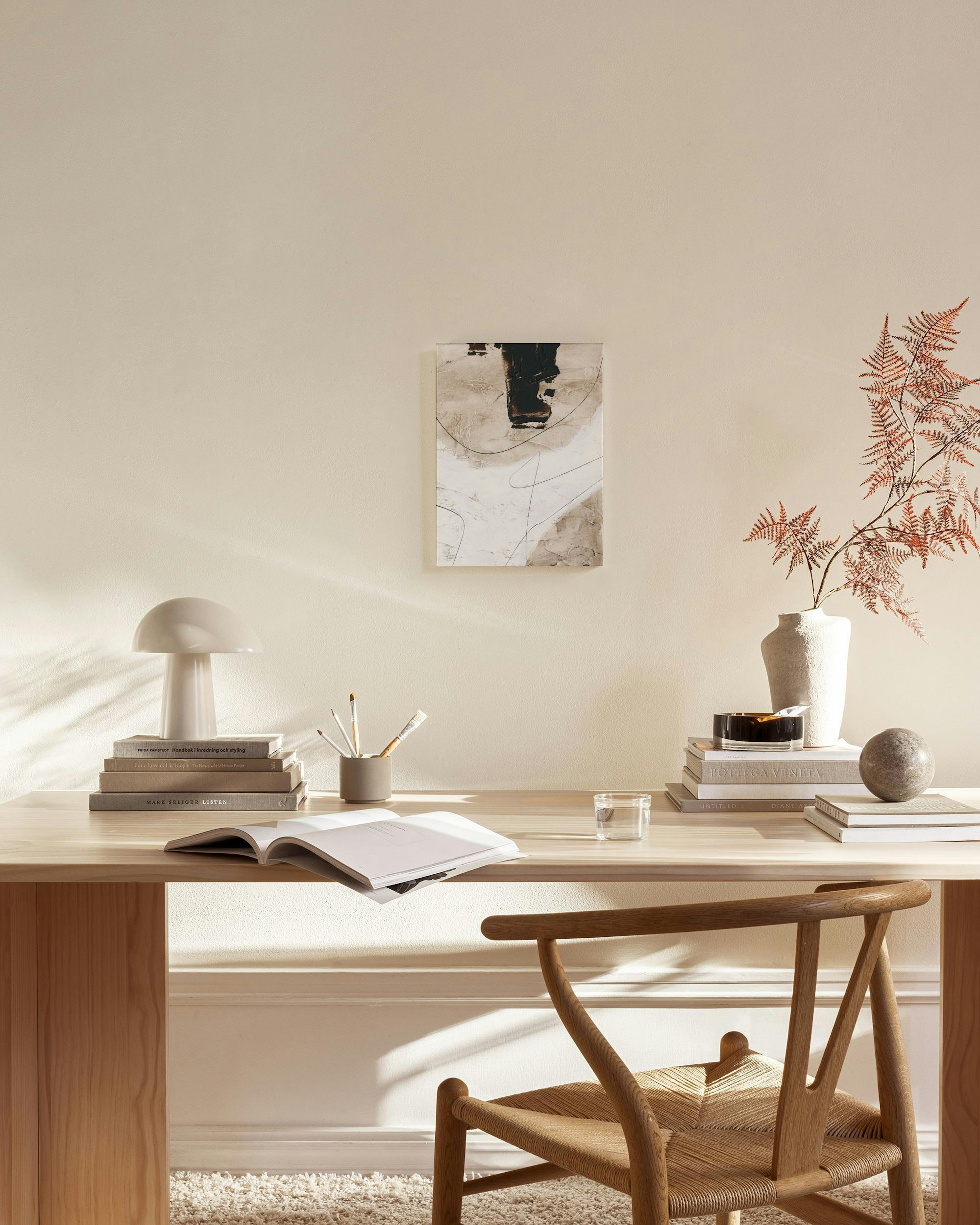 Abstract print with black, beige, and white brushstrokes and thin lines, hanging in a minimalist living room.