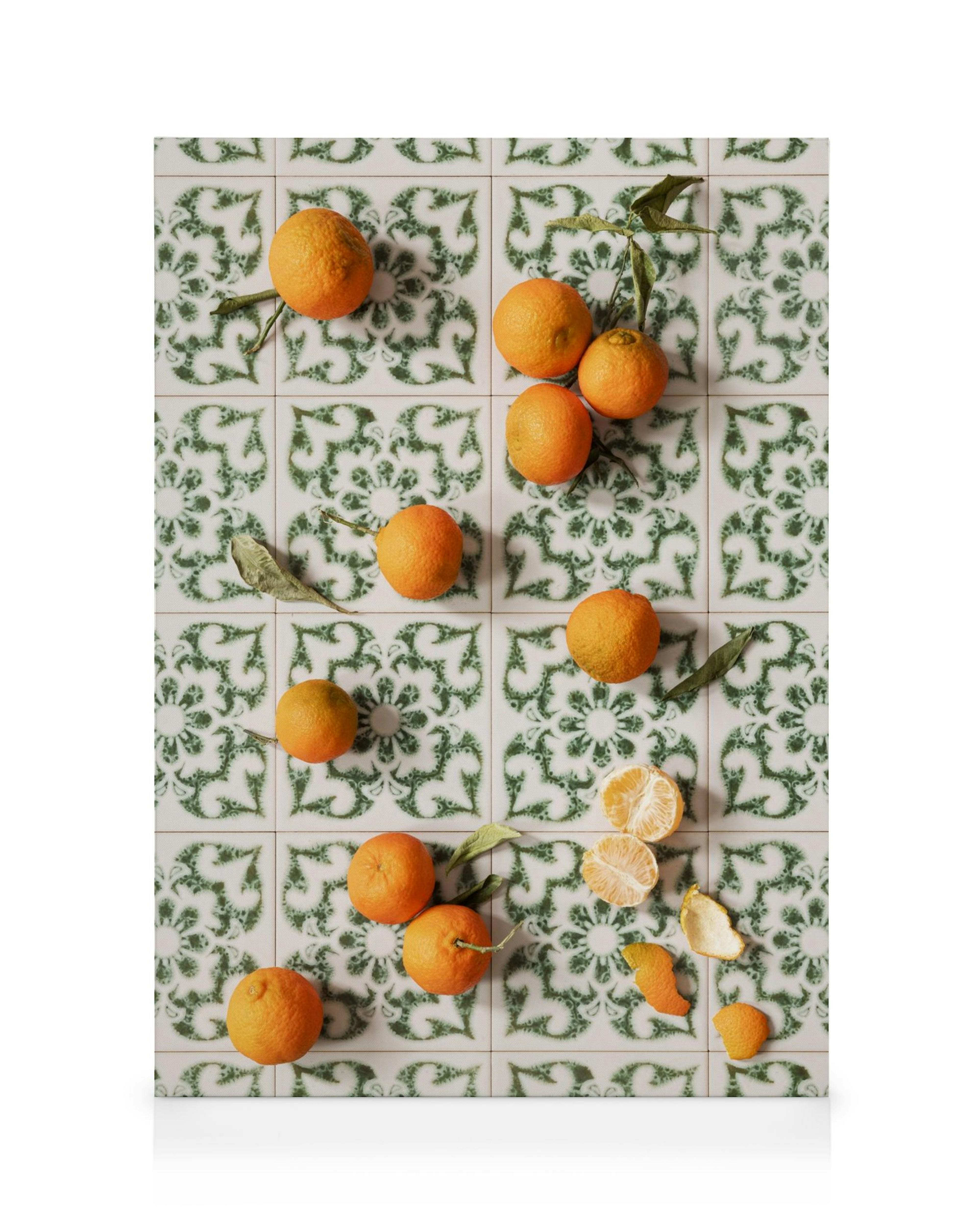 En canvastavla med apelsiner och mandariner på ett vitt kakel med grönt mönster.