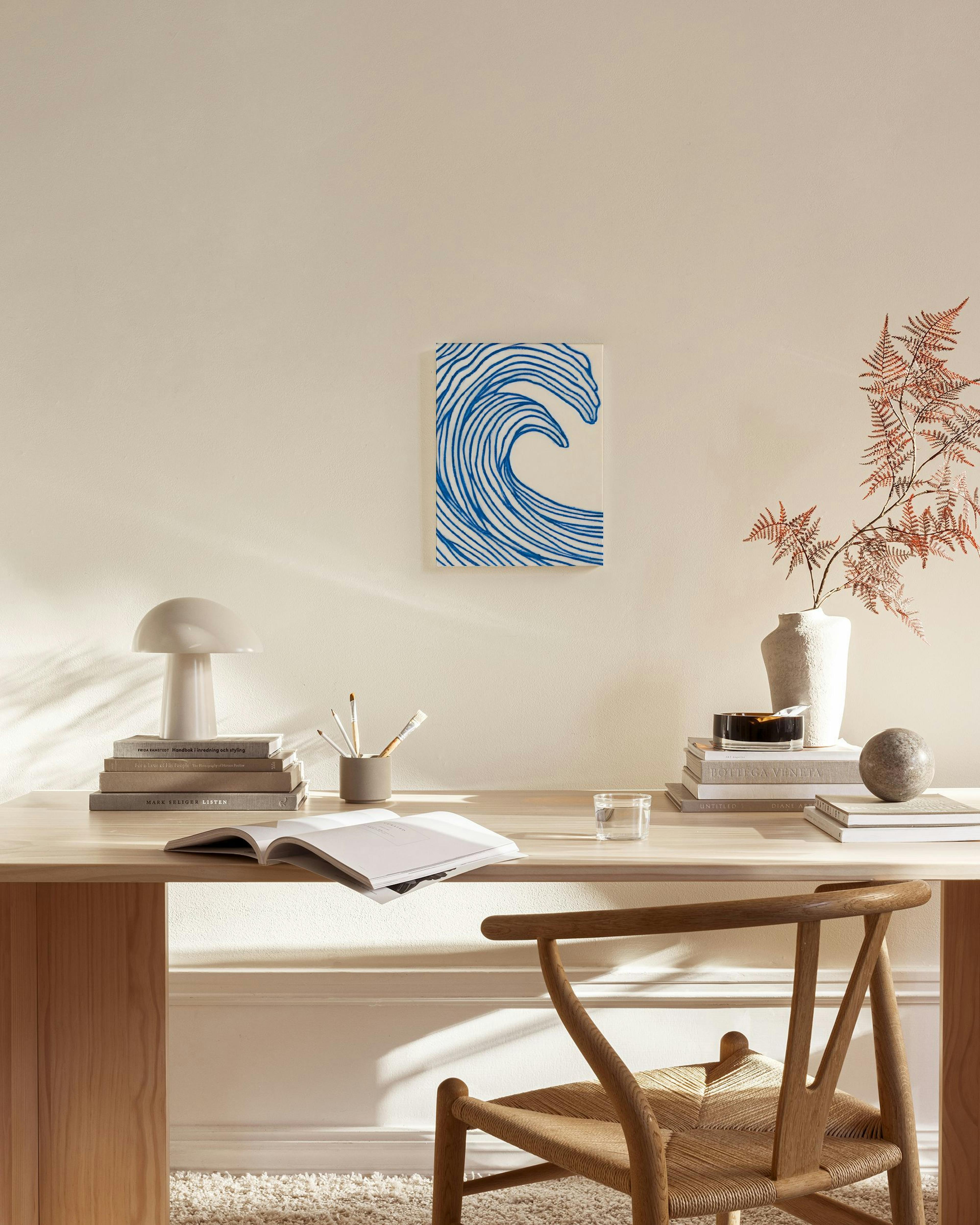 A canvas print of a blue abstract wave on a light background, hanging in a modern living room above a wooden console.