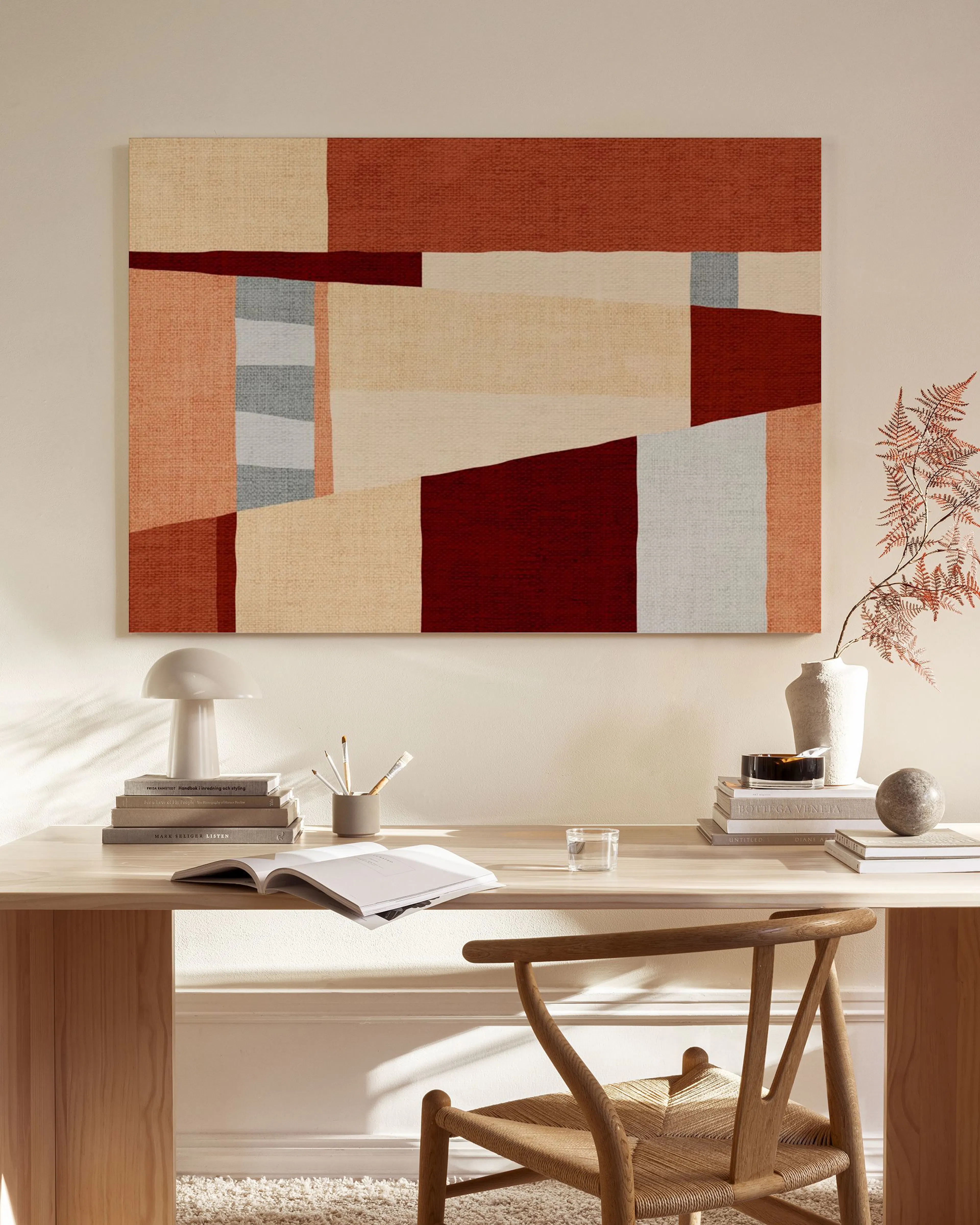 Canvas met abstracte vormen in aardetinten zoals rood, beige en grijs, hangend boven een houten dressoir in een modern interieur