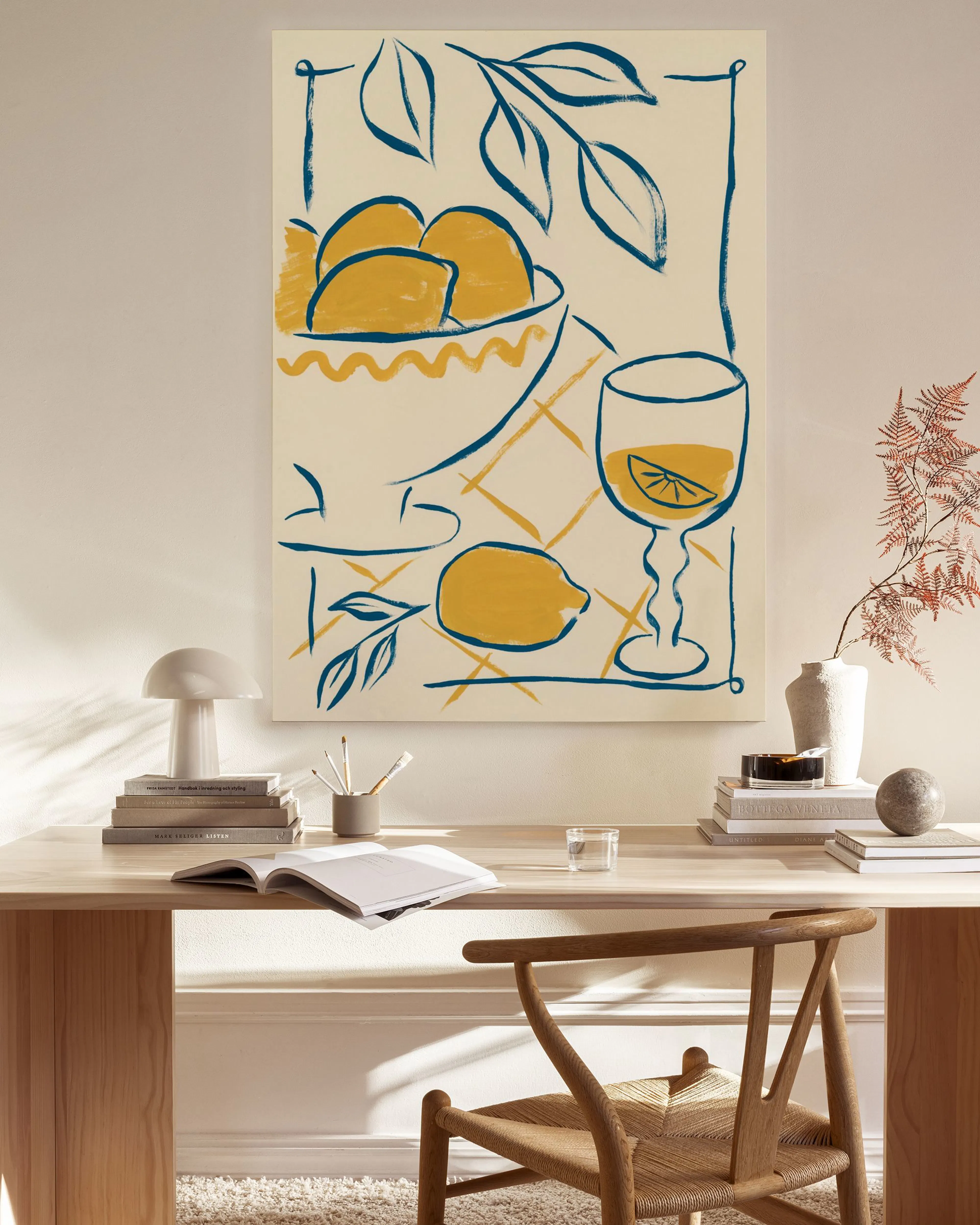 Leinwandbild mit Zitronen und Weinglas in Blau und Gelb, im hellen Wohnzimmer über einem Sideboard.
