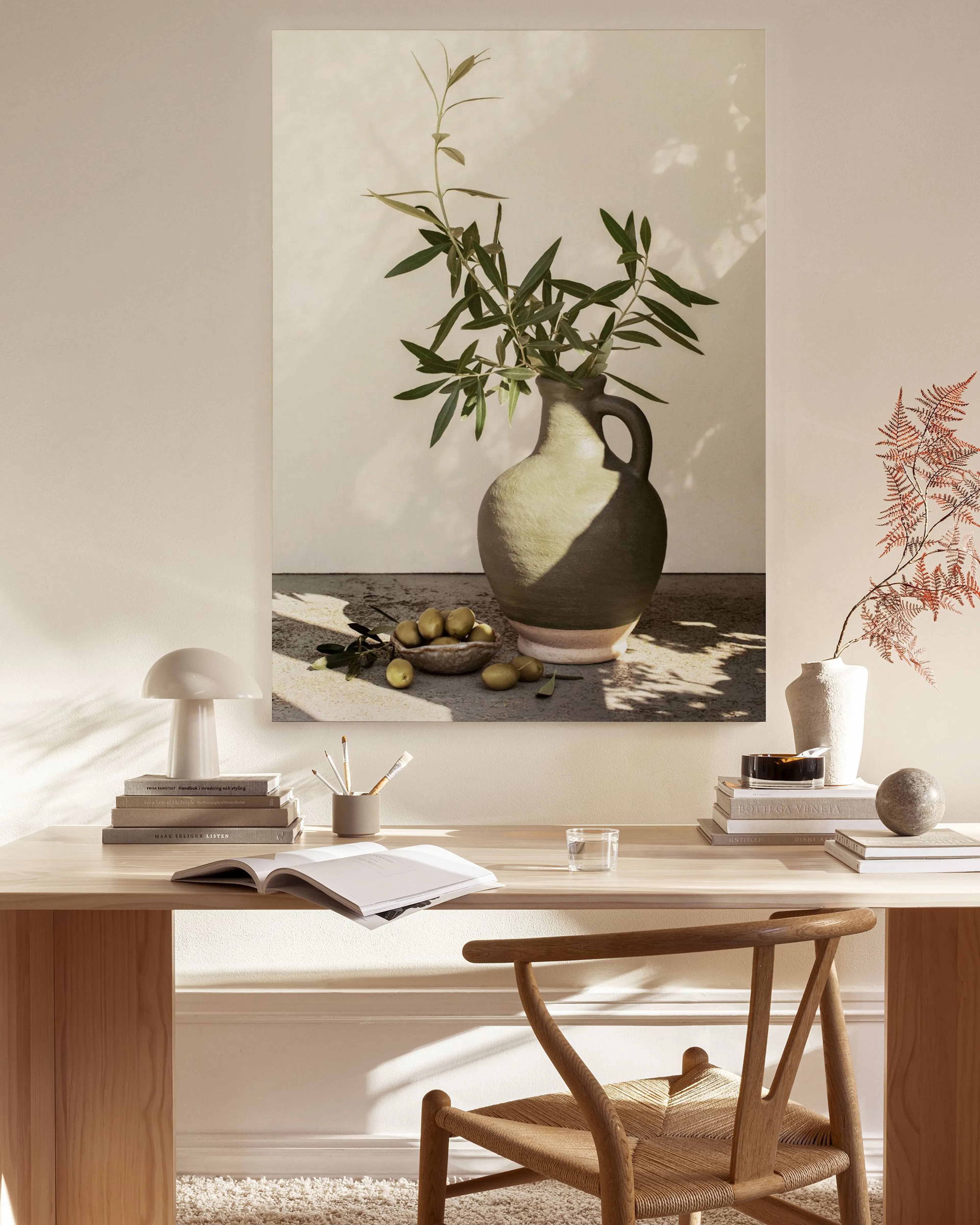 Leinwandbild mit Olivenbaumzweigen in Vase, Oliven und Schatten, hängt über einem Sideboard im Wohnzimmer.