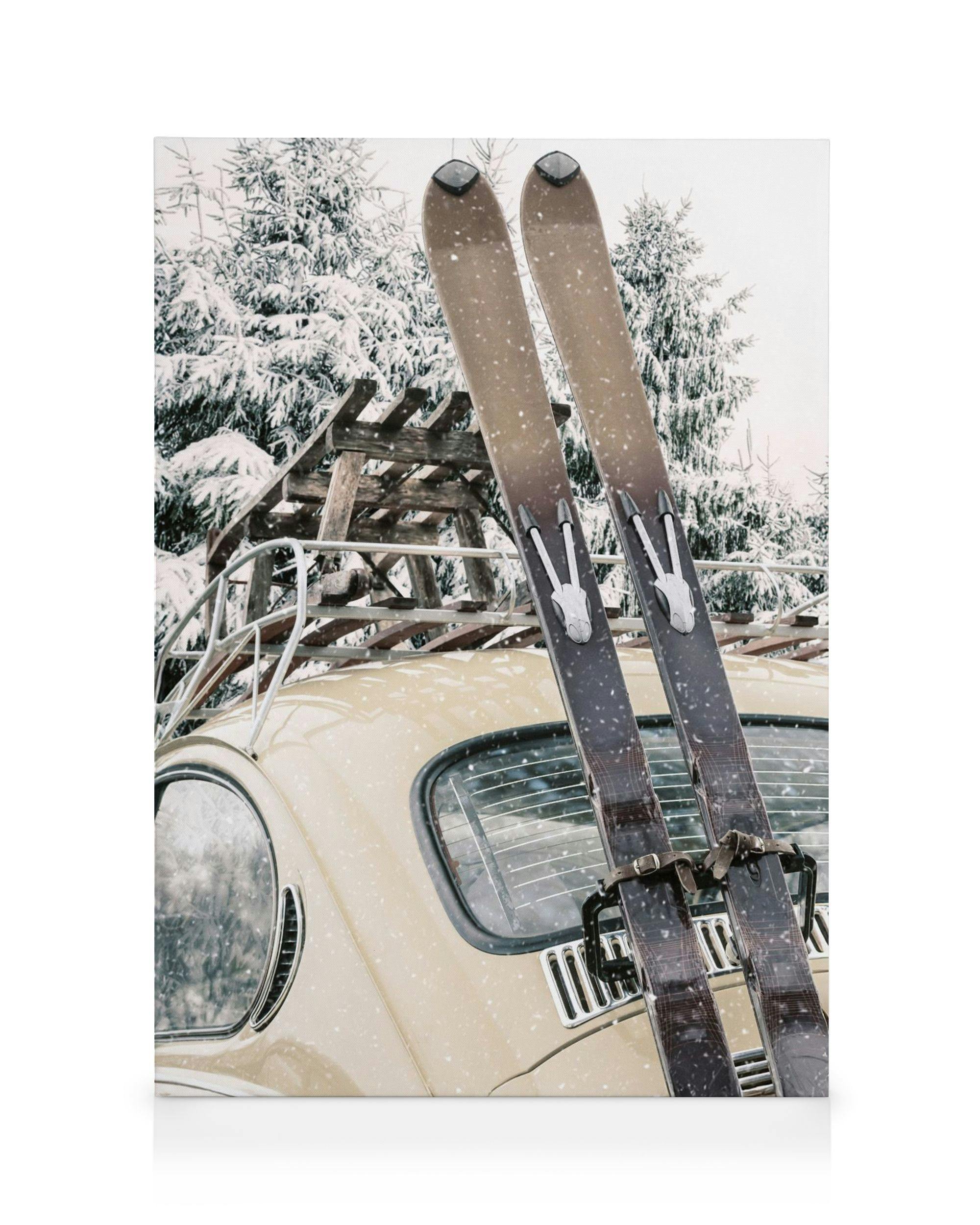 Stampa su tela di sci vintage legati sul retro di unauto depoca color crema in un paesaggio innevato.