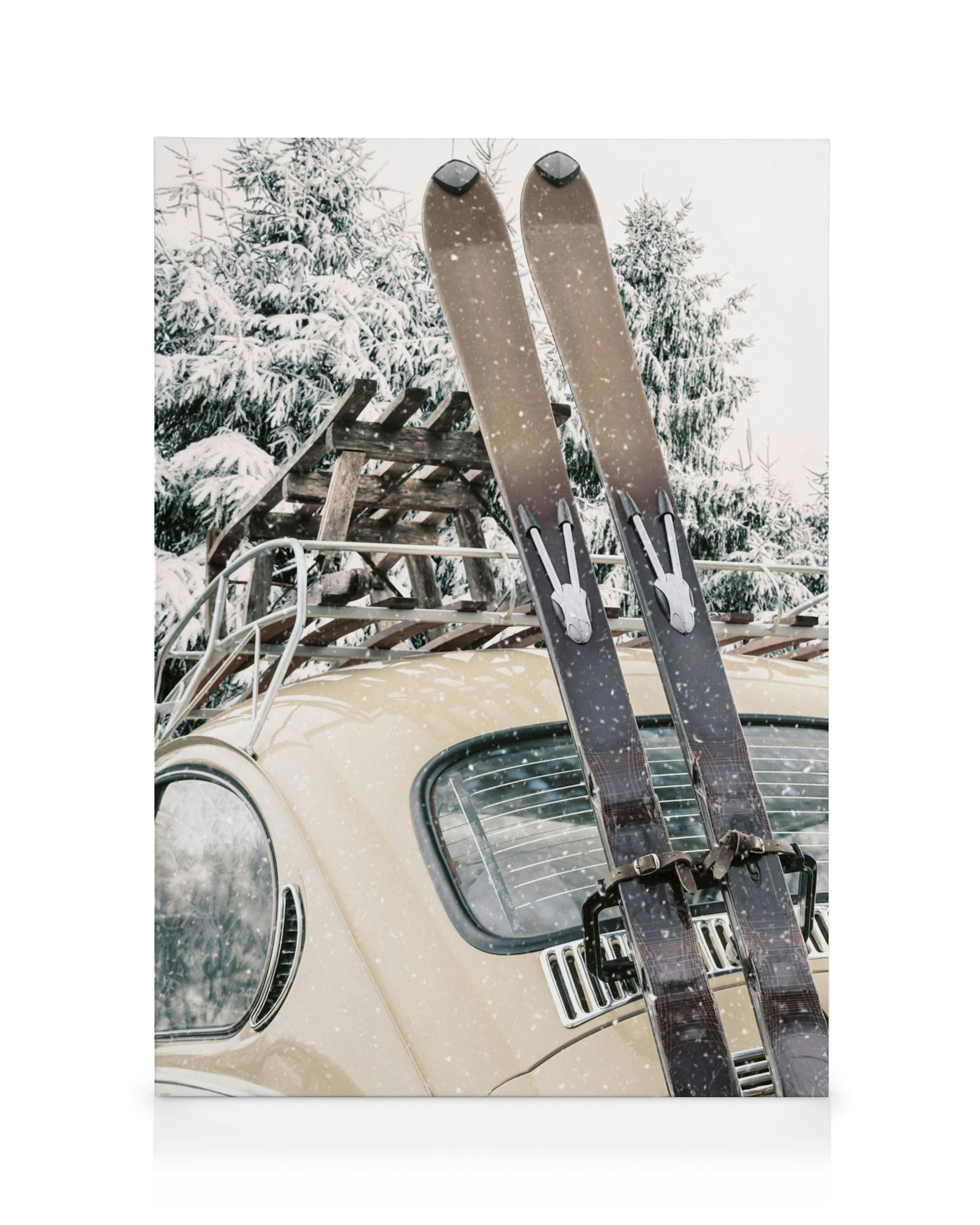 Stampa su tela di sci vintage legati sul retro di unauto depoca color crema in un paesaggio innevato.