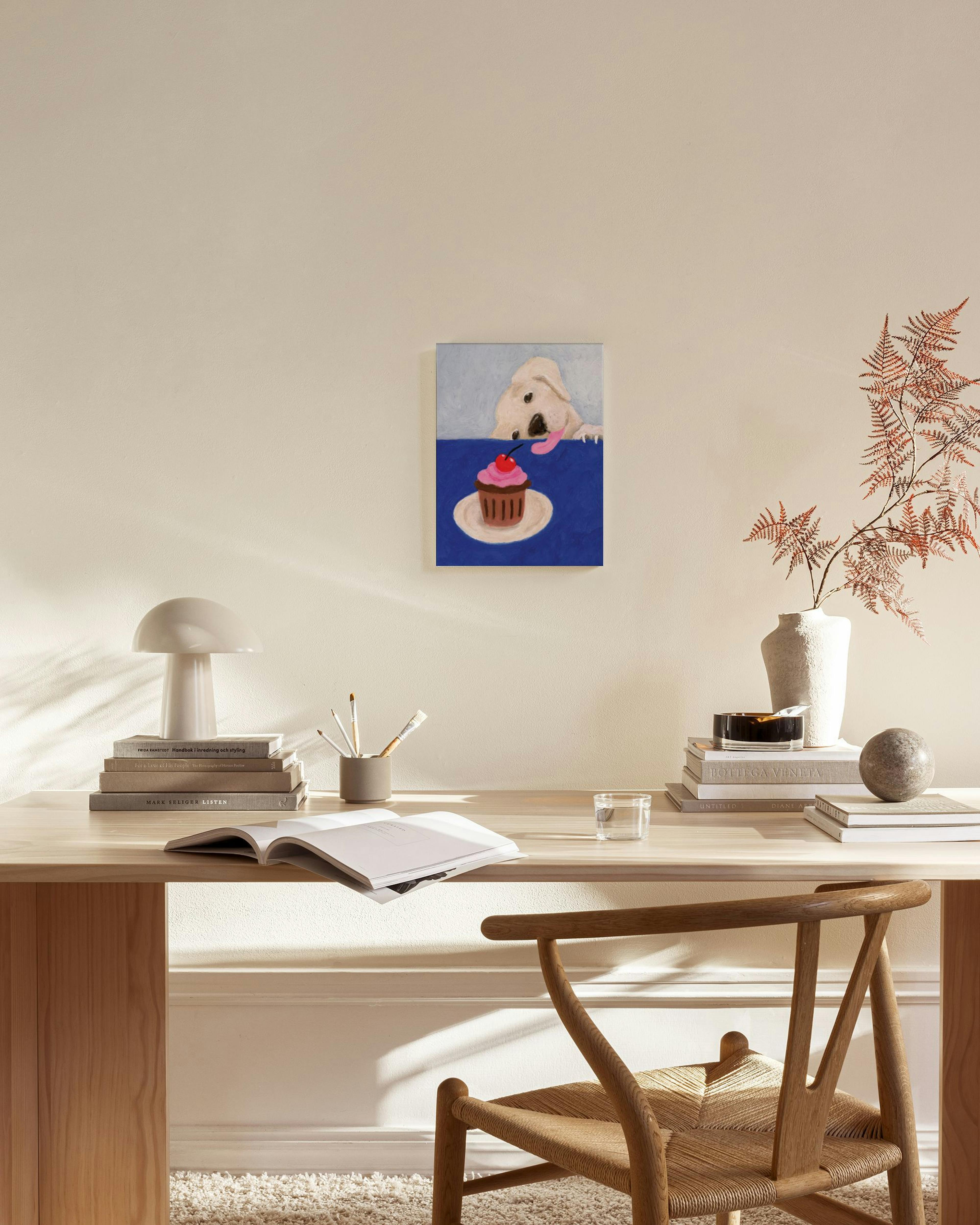 Obraz na płótnie z psem patrzącym na babeczkę z wisienką, zawieszony w jasnym salonie nad komodą.