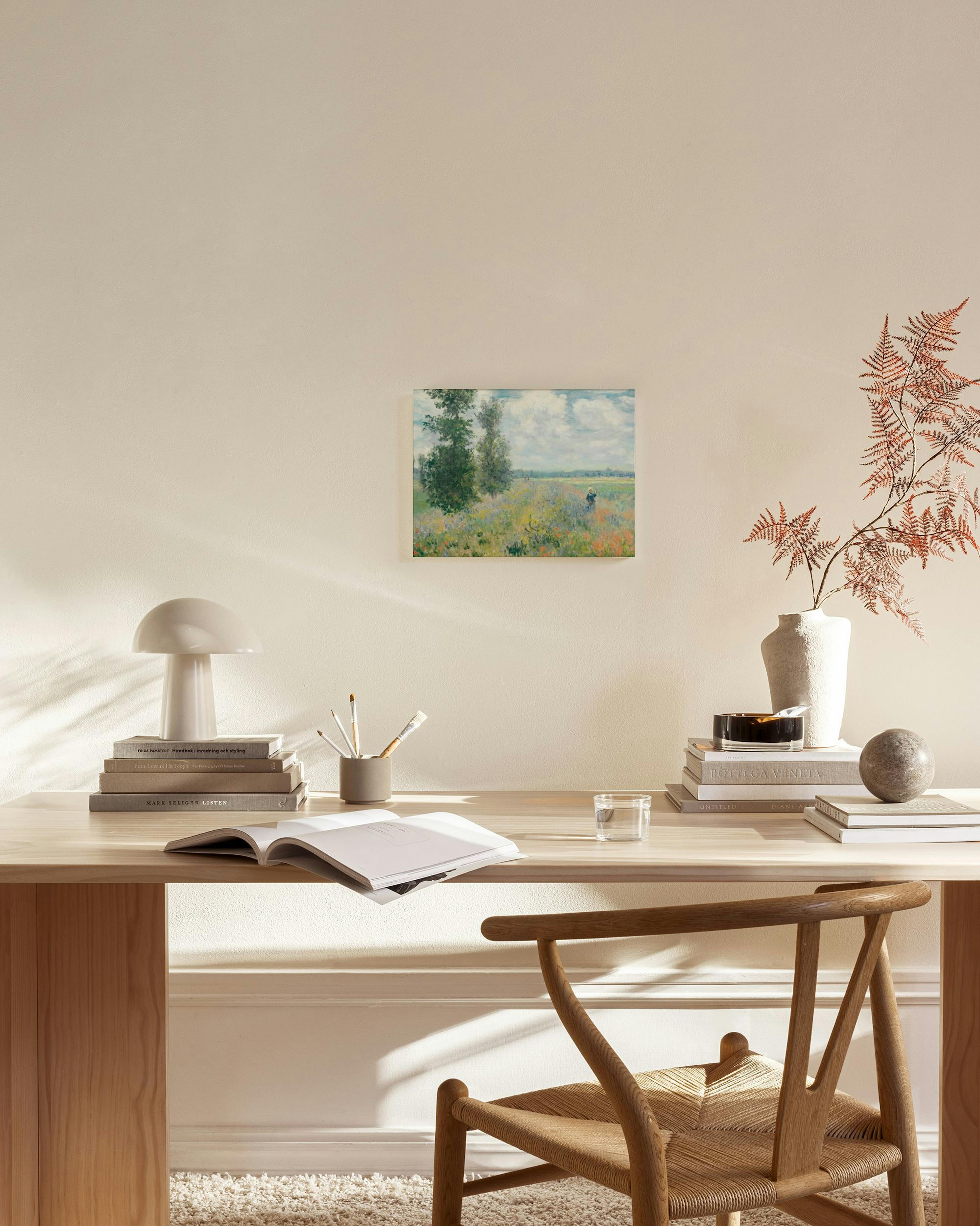 Tela decorativa com paisagem de prado florido e árvores, pendurada numa sala de estar minimalista com móveis de madeira.