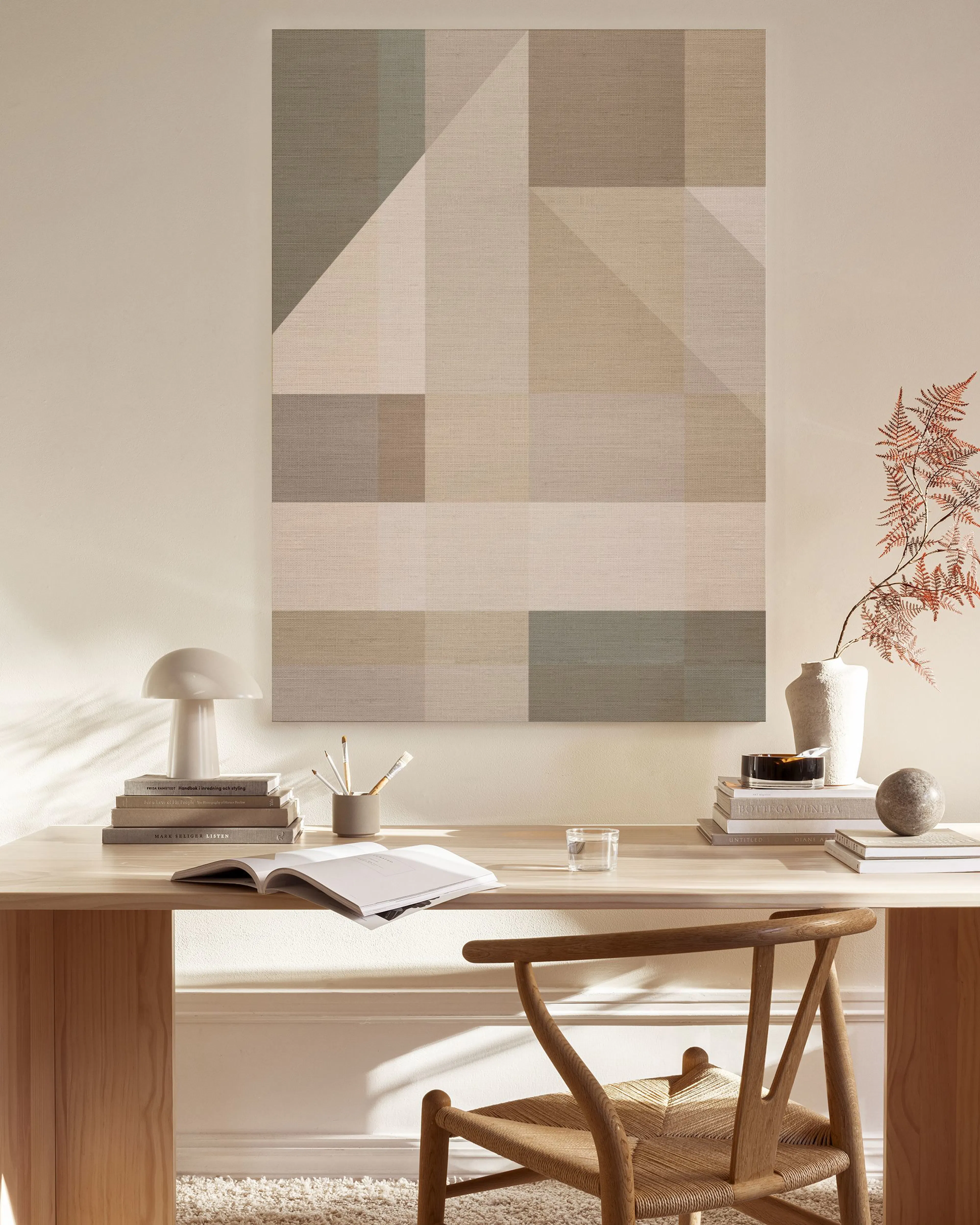 Lerretsbilde med geometriske former i beige og gråtoner, henger over et lavt skap i en moderne stue med lenestol.