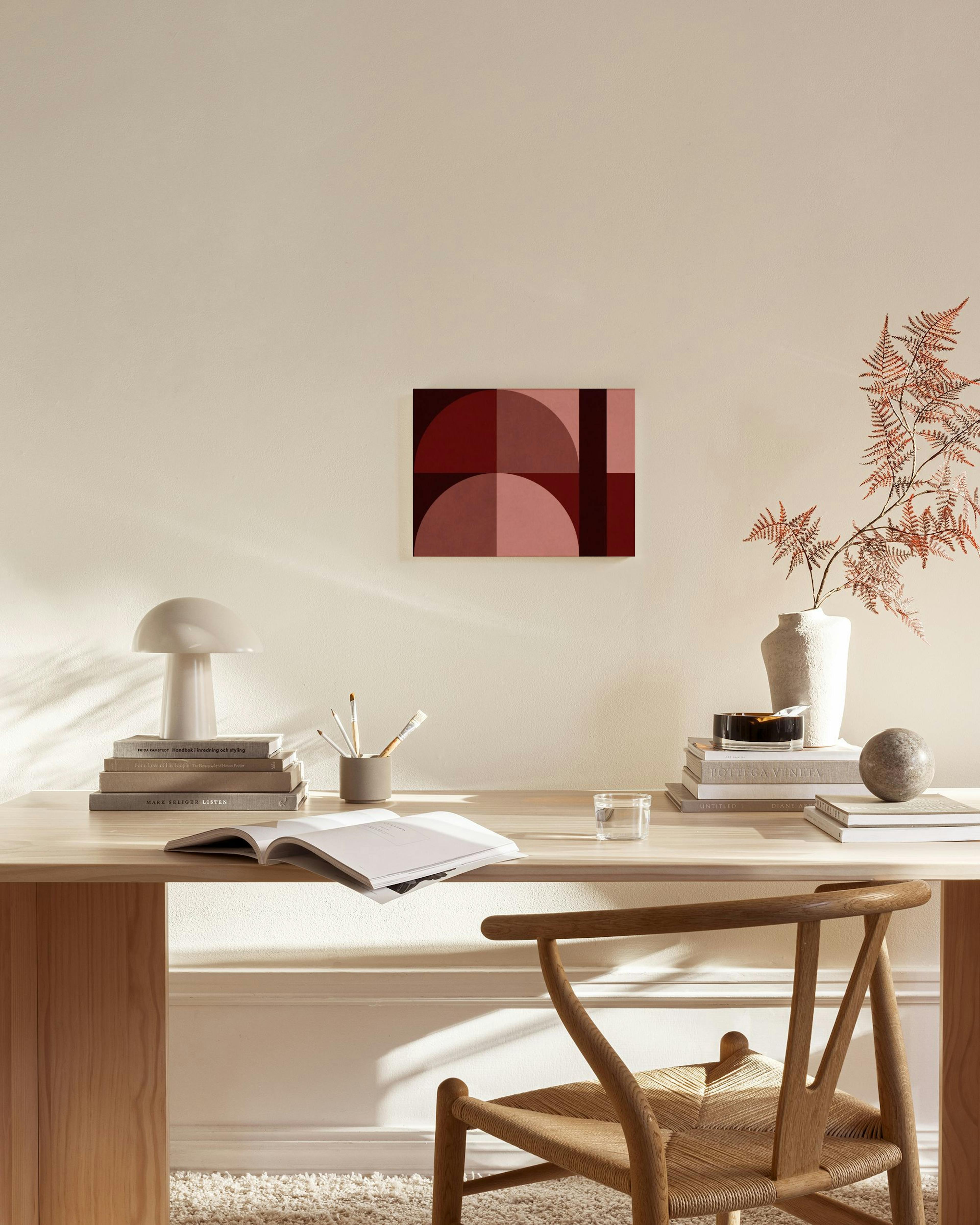 Lienzo de formas geométricas en tonos rojos y rosados, colgado en una sala de estar moderna sobre un mueble de madera.