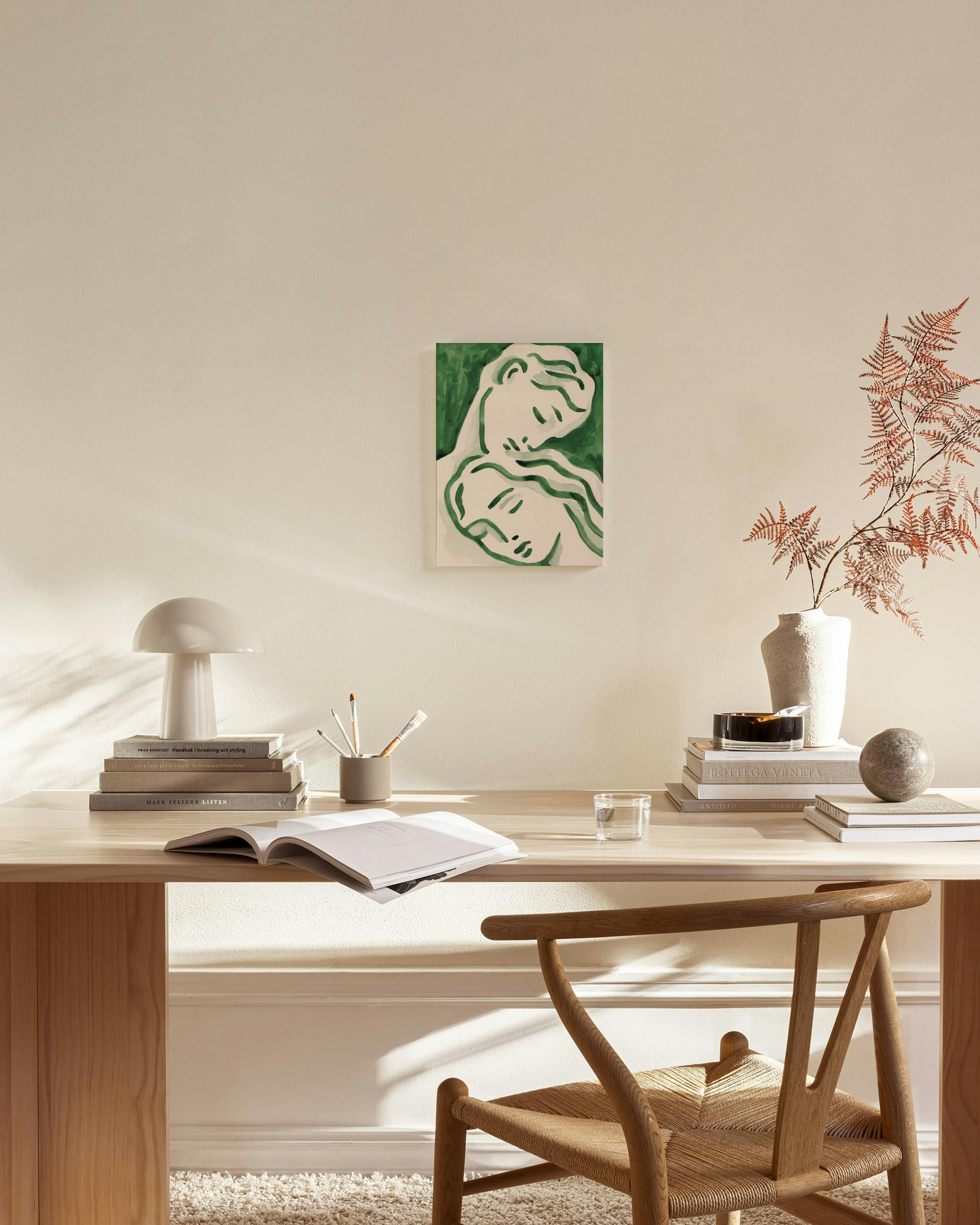 Lerretsbilde med ansikter i grønne og beige nyanser, henger i en lys, moderne stue over en trebenk.