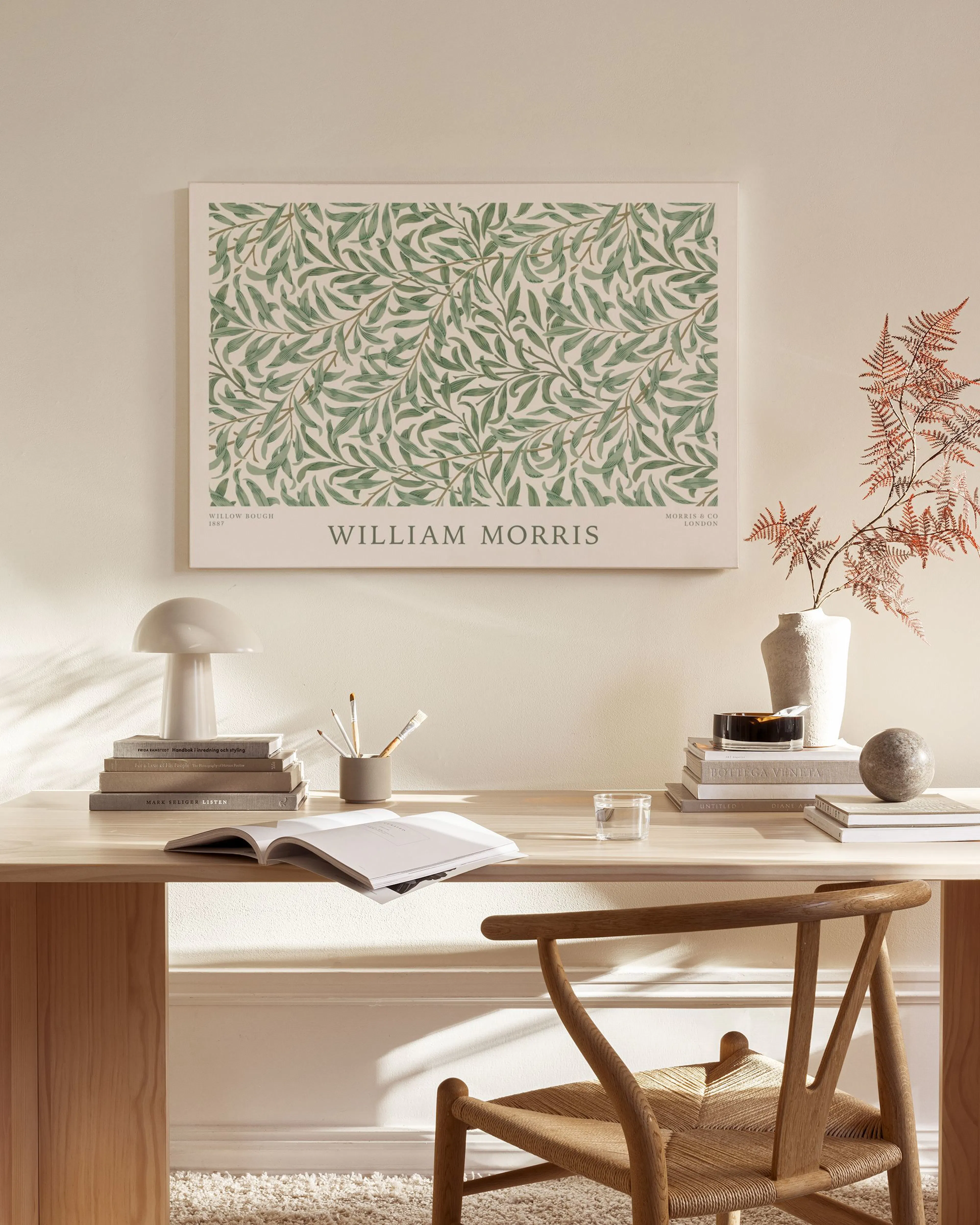 Canvastavla med gröna löv på en ljus bakgrund och texten William Morris, hänger ovanför en tv-bänk i ett ljust vardagsrum.