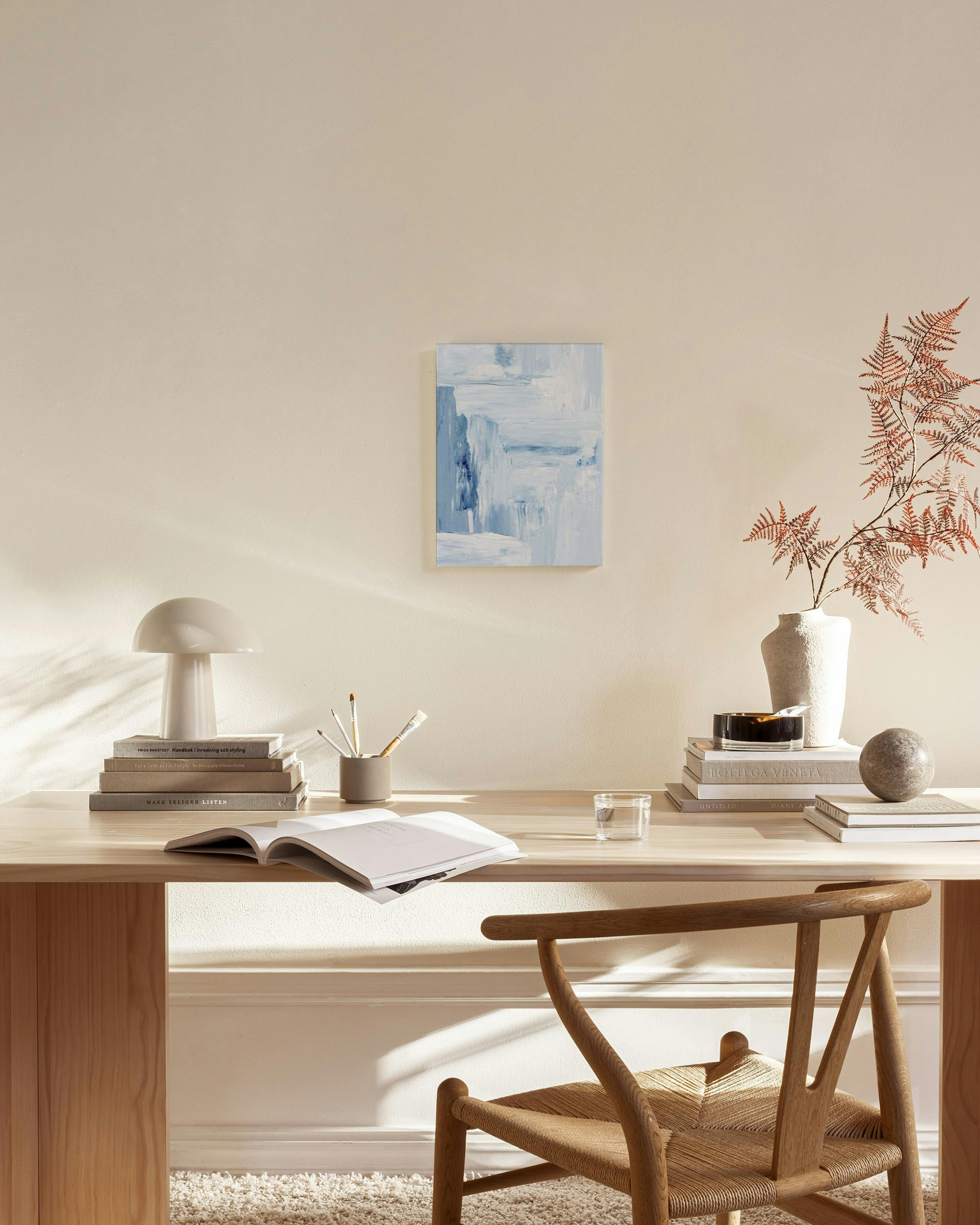 Tela decorativa abstrata com tons de azul claro e branco, pendurada numa sala de estar moderna com móveis de madeira e tons neut