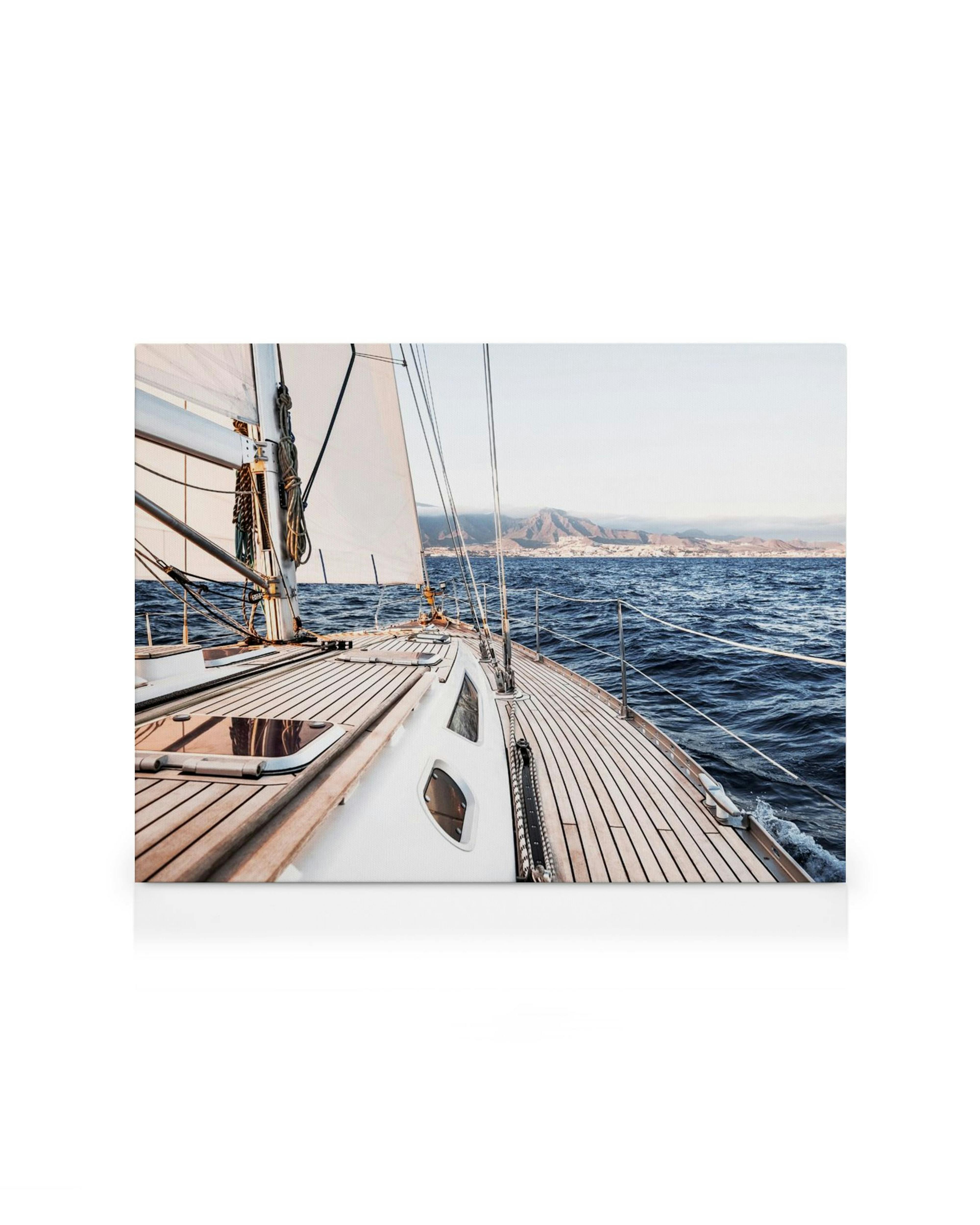 Cubierta de velero con velas desplegadas sobre olas azules, montañas a lo lejos bajo un cielo claro. Arte marino.