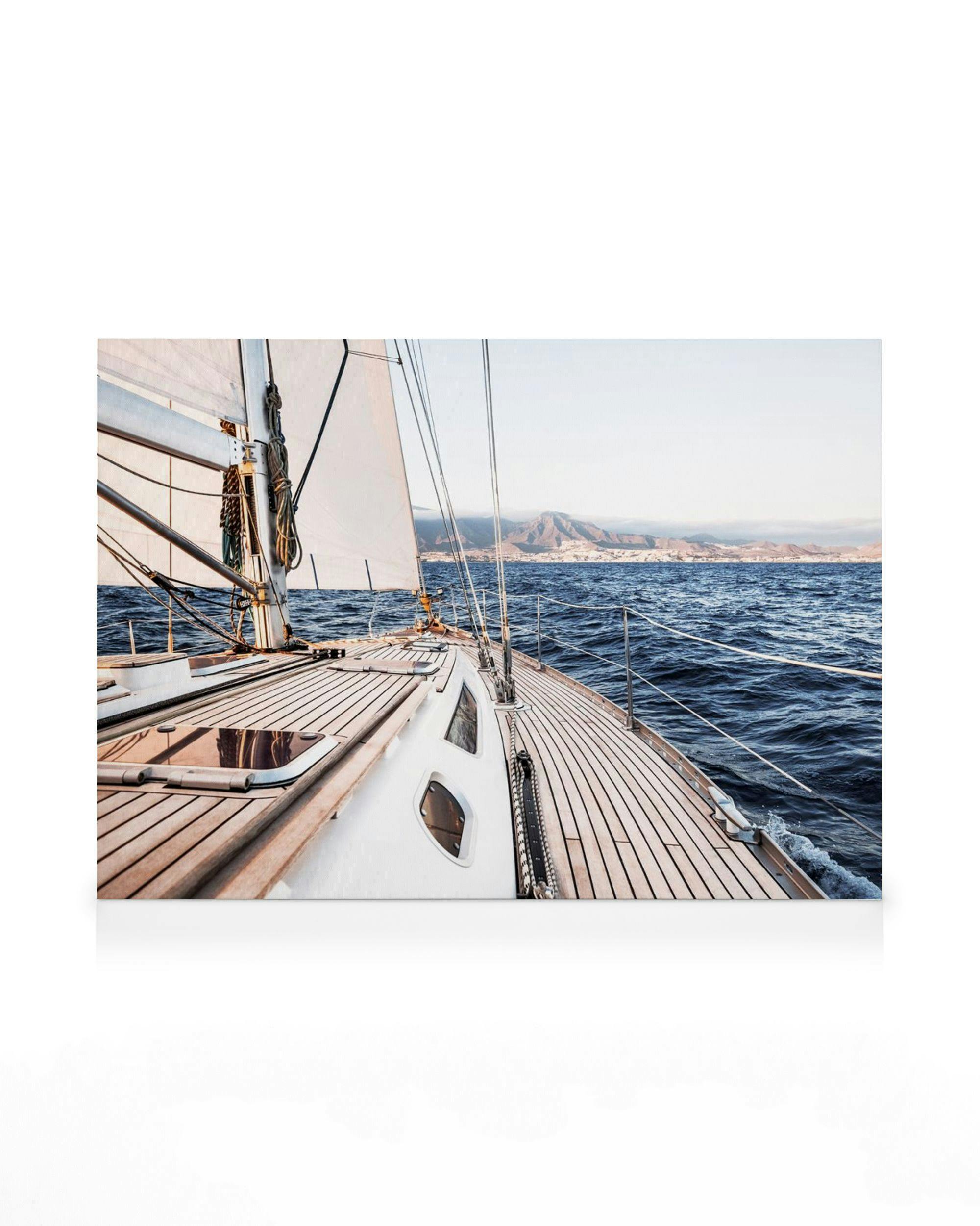 Sailboat deck with wooden floors, white sails, blue water, and distant mountains under a light sky.