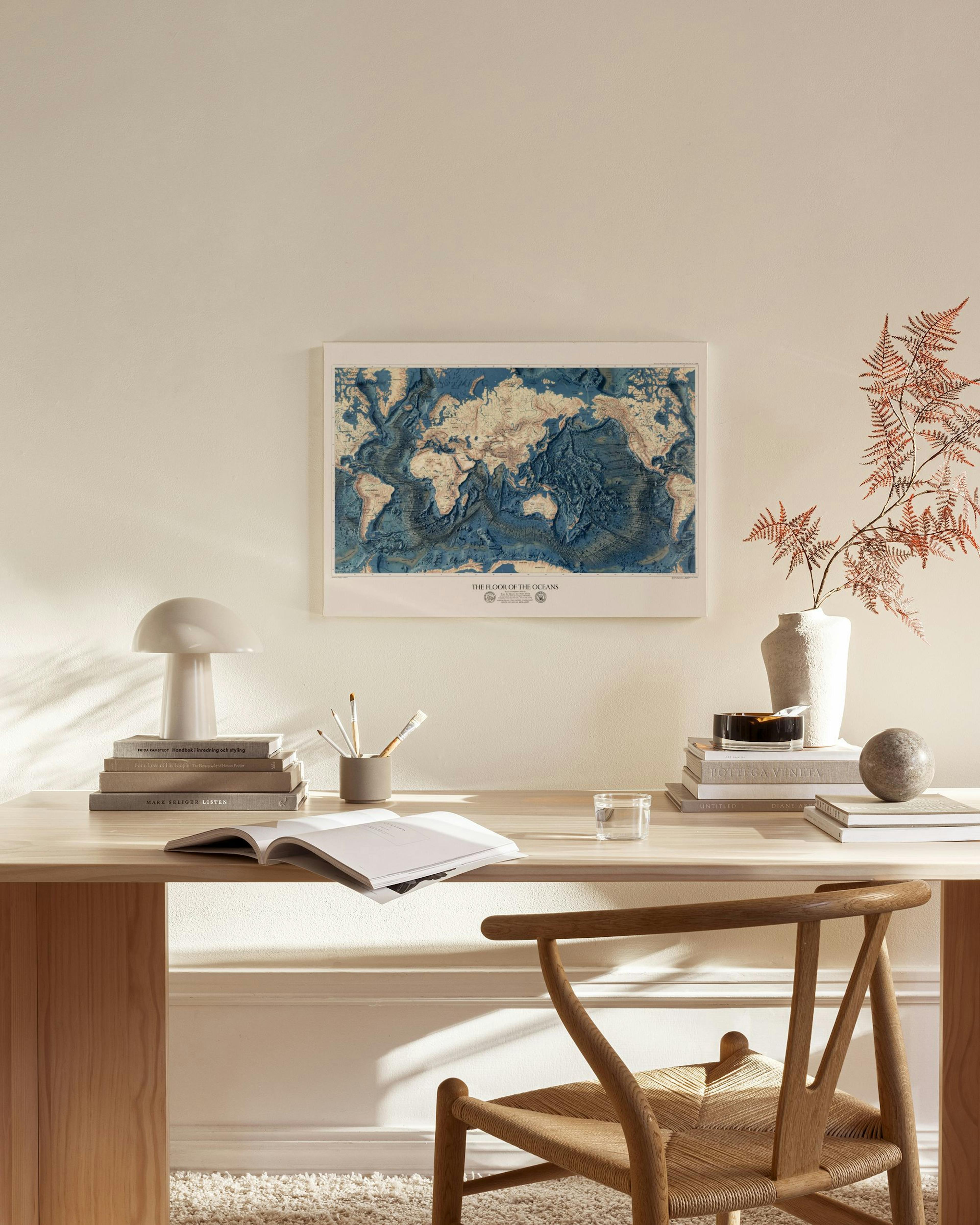 Lærred med verdenskort i blå og beige nuancer, hængende i en stue over et træmøbel.