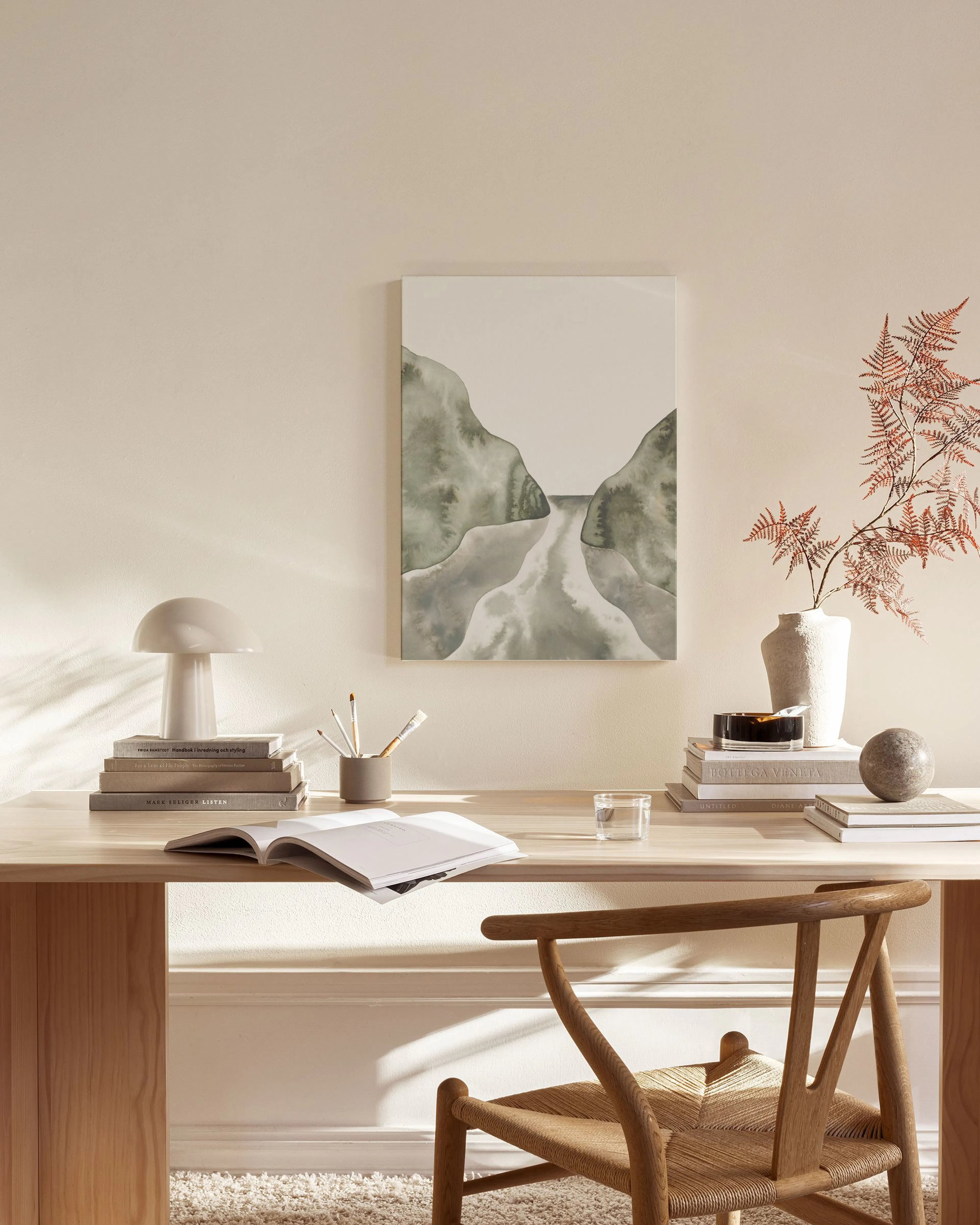 Leinwandbild mit abstraktem Flusslauf zwischen grünen Hügeln, hängend über einem Sideboard in einem beigen Wohnzimmer.
