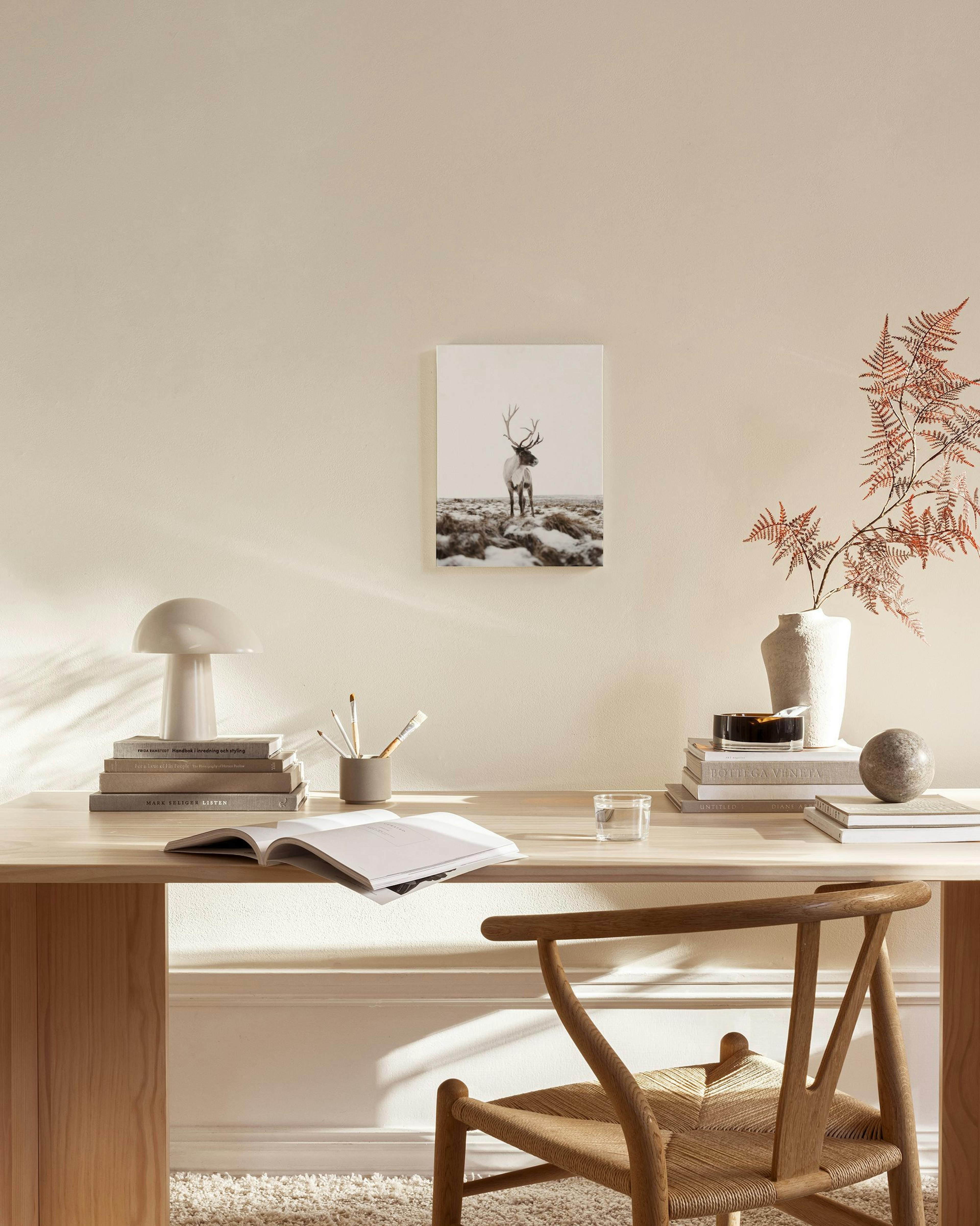 Canvas van een rendier in een besneeuwd landschap, hangend in een lichte, moderne woonkamer boven een houten dressoir.