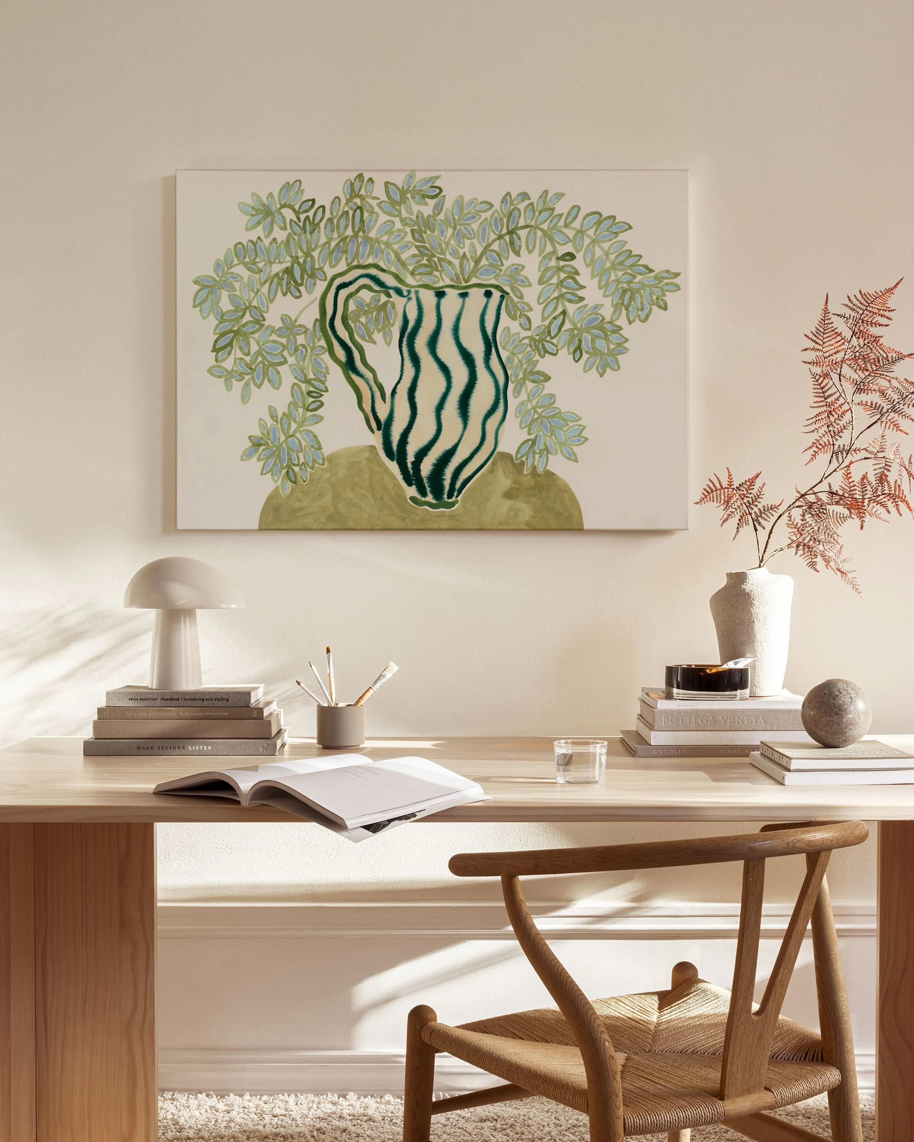 A canvas print of a green and white striped vase with lush green foliage, hanging above a wooden sideboard in a modern living ro