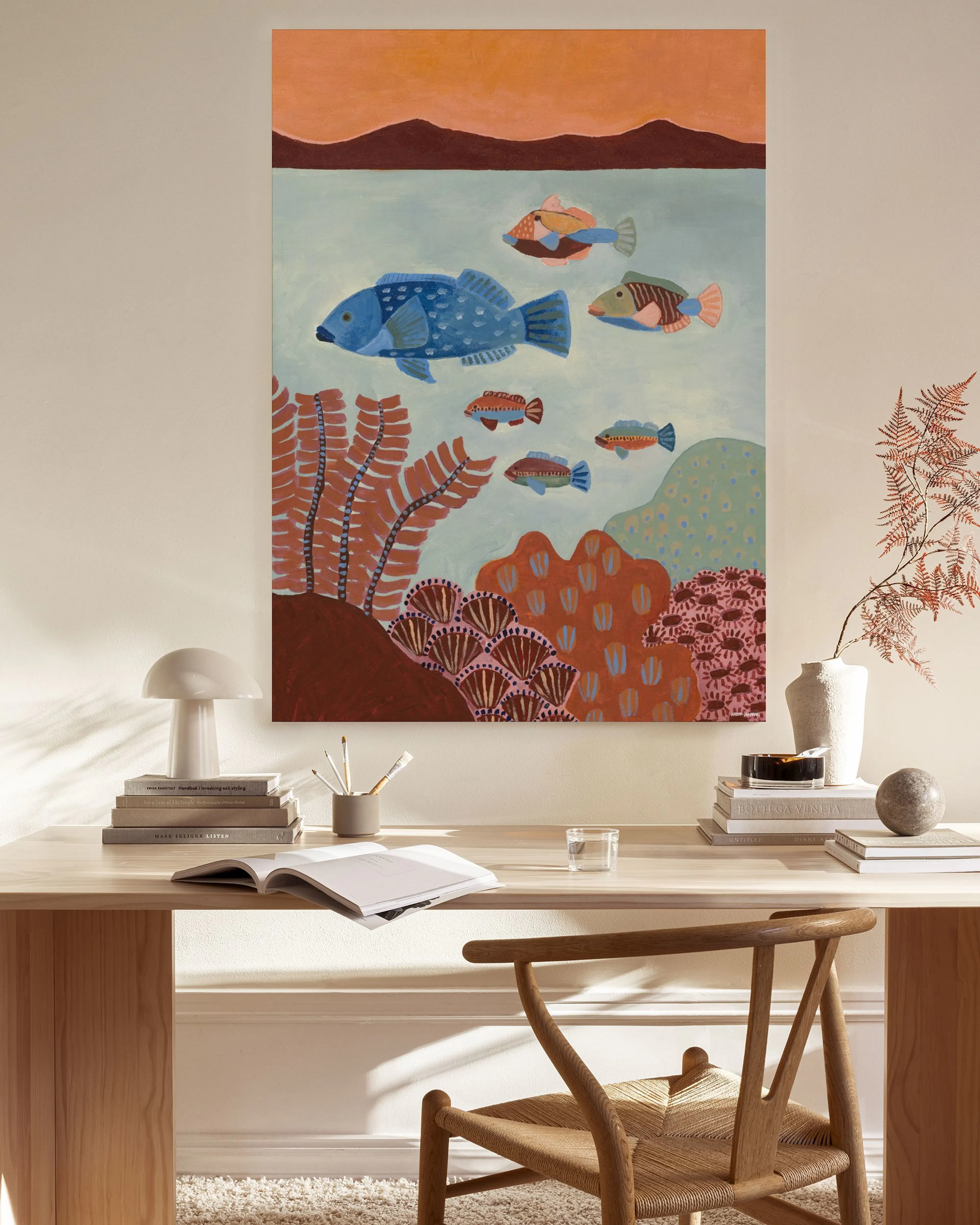 Lienzo con ilustración de peces azules y marrones en un arrecife, colgando en un salón con muebles de madera clara.