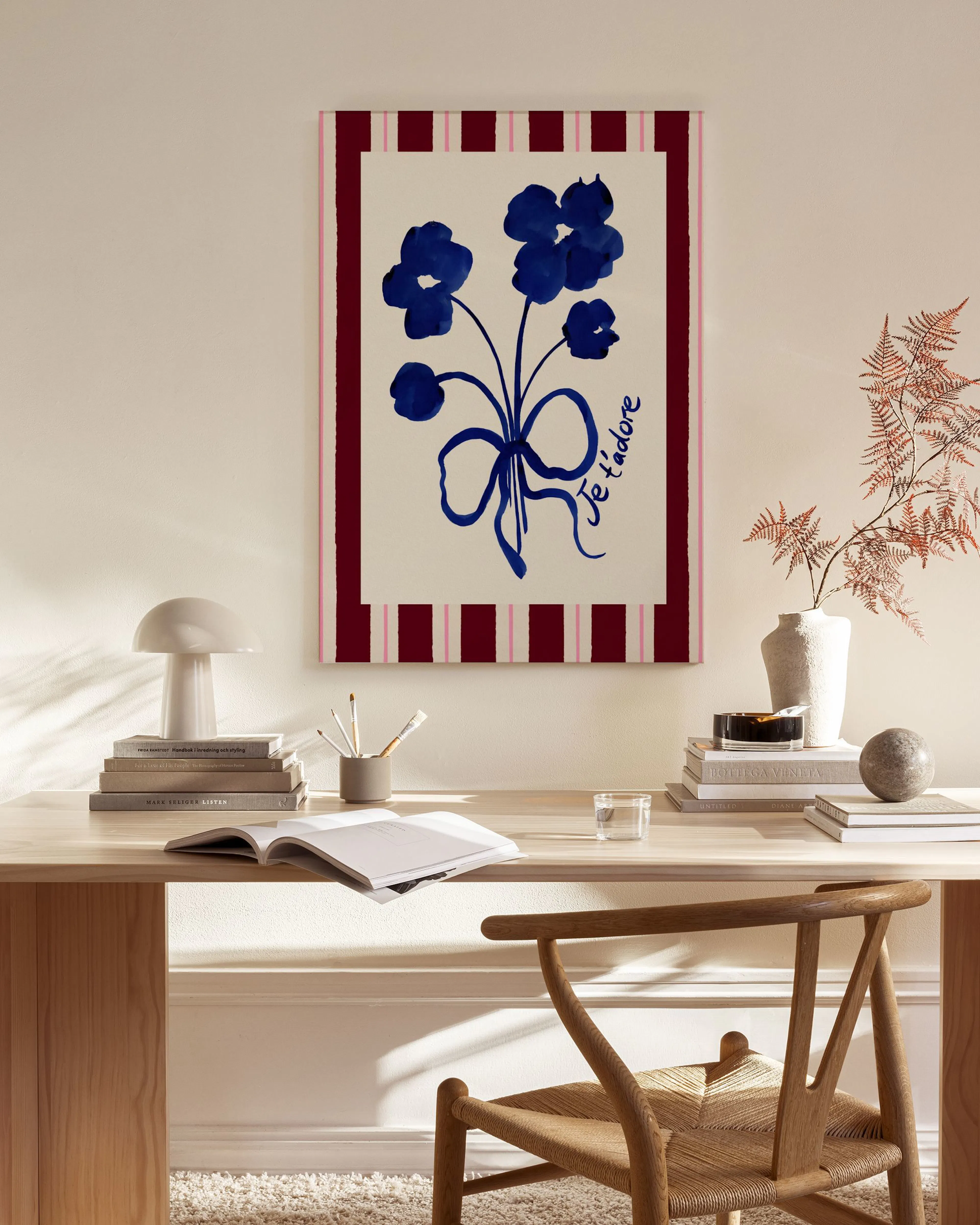 A canvas print of blue flowers with a bow and Je tadore text on a red and white striped background, hanging in a minimalist livi
