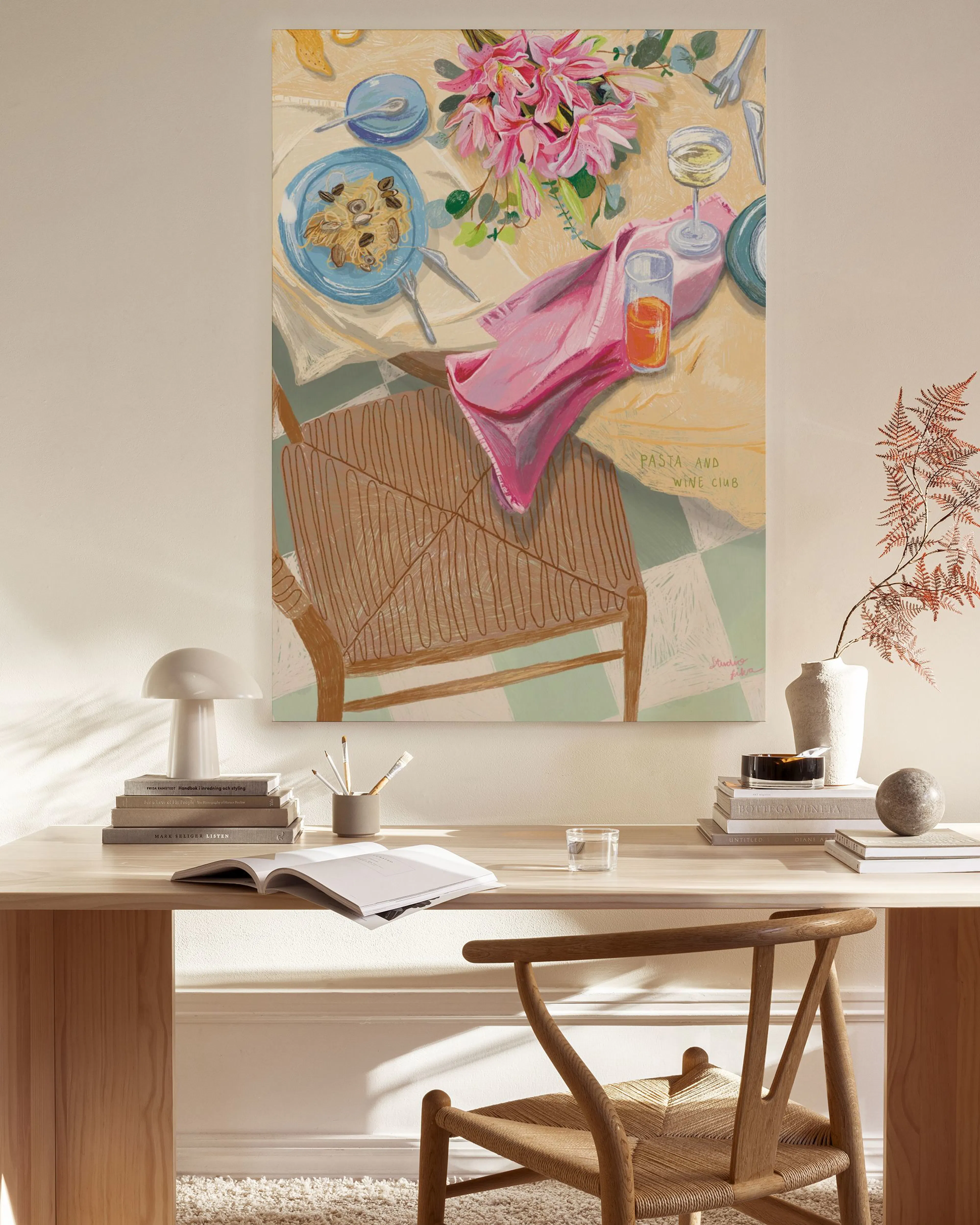 Lerretsbilde med et fargerikt motiv av et bord dekket med mat, blomster og drikke, henger i en lys stue.