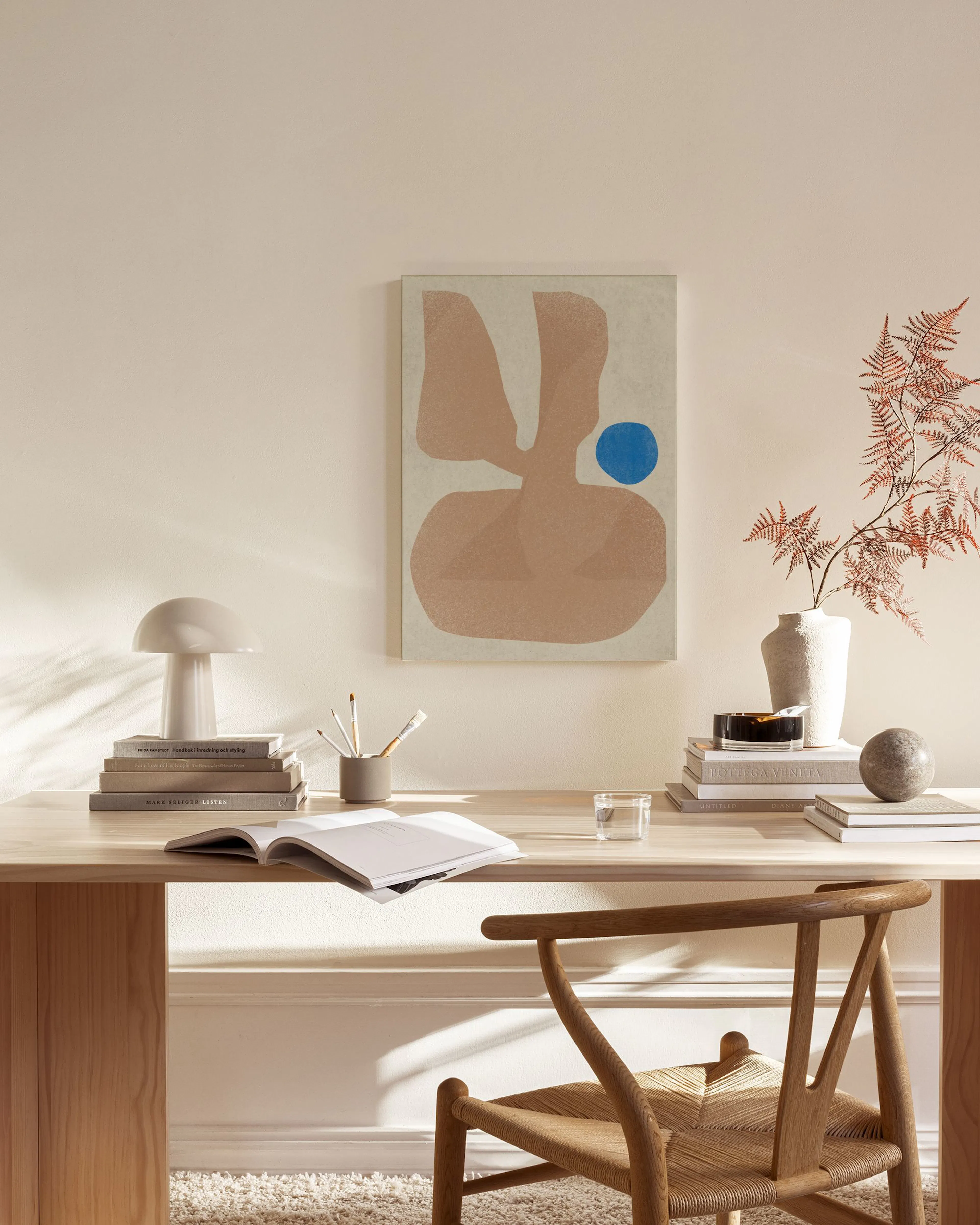 Abstract canvas print with large organic beige and brown shapes, and a small blue circle, hanging in a minimalist living room.