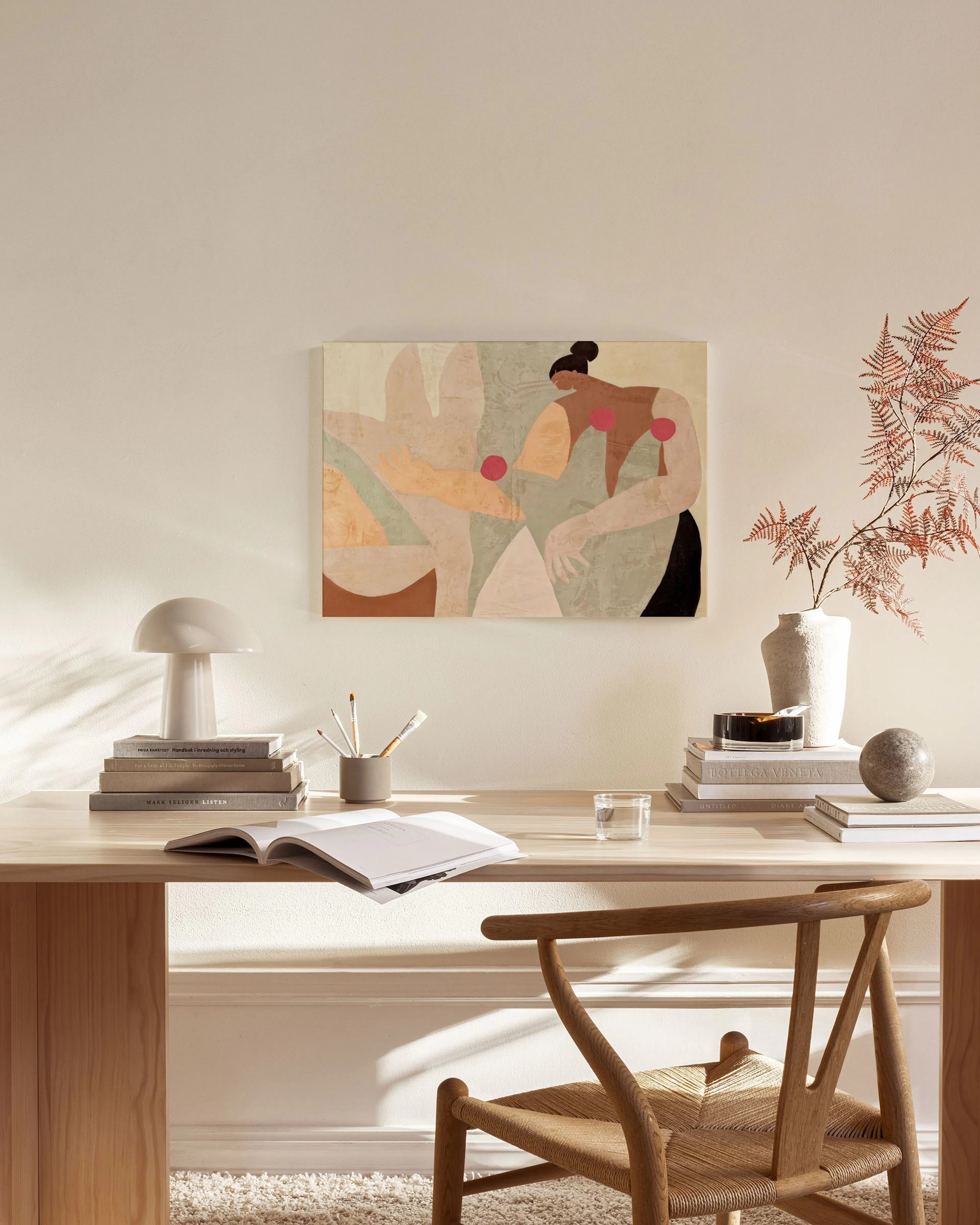Lærred med abstrakt kunst af to kvindelige figurer i varme farver, ophængt i en minimalistisk stue.