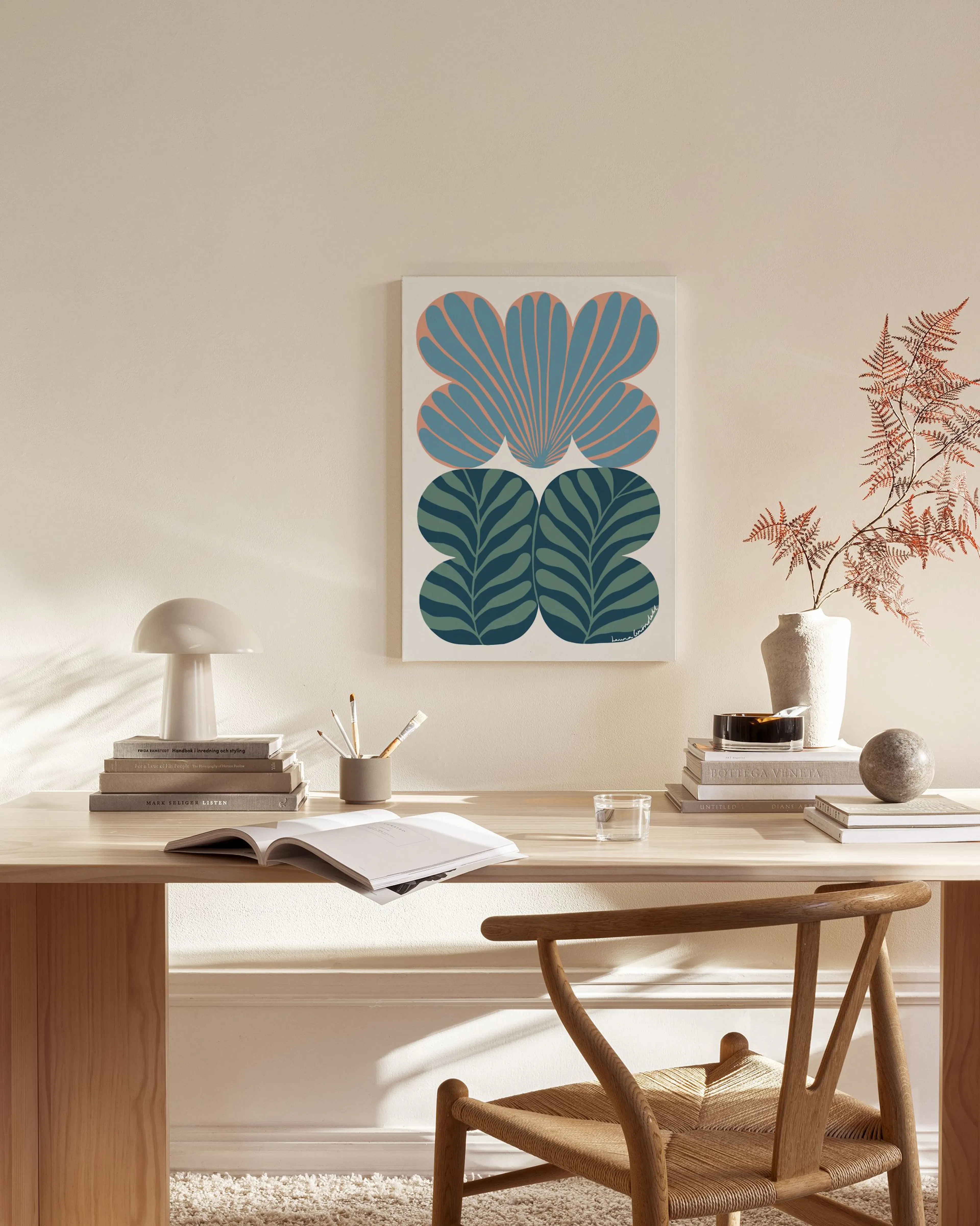 A canvas print with blue shell-like shapes and green botanical patterns, hanging in a bright, minimalist living room.